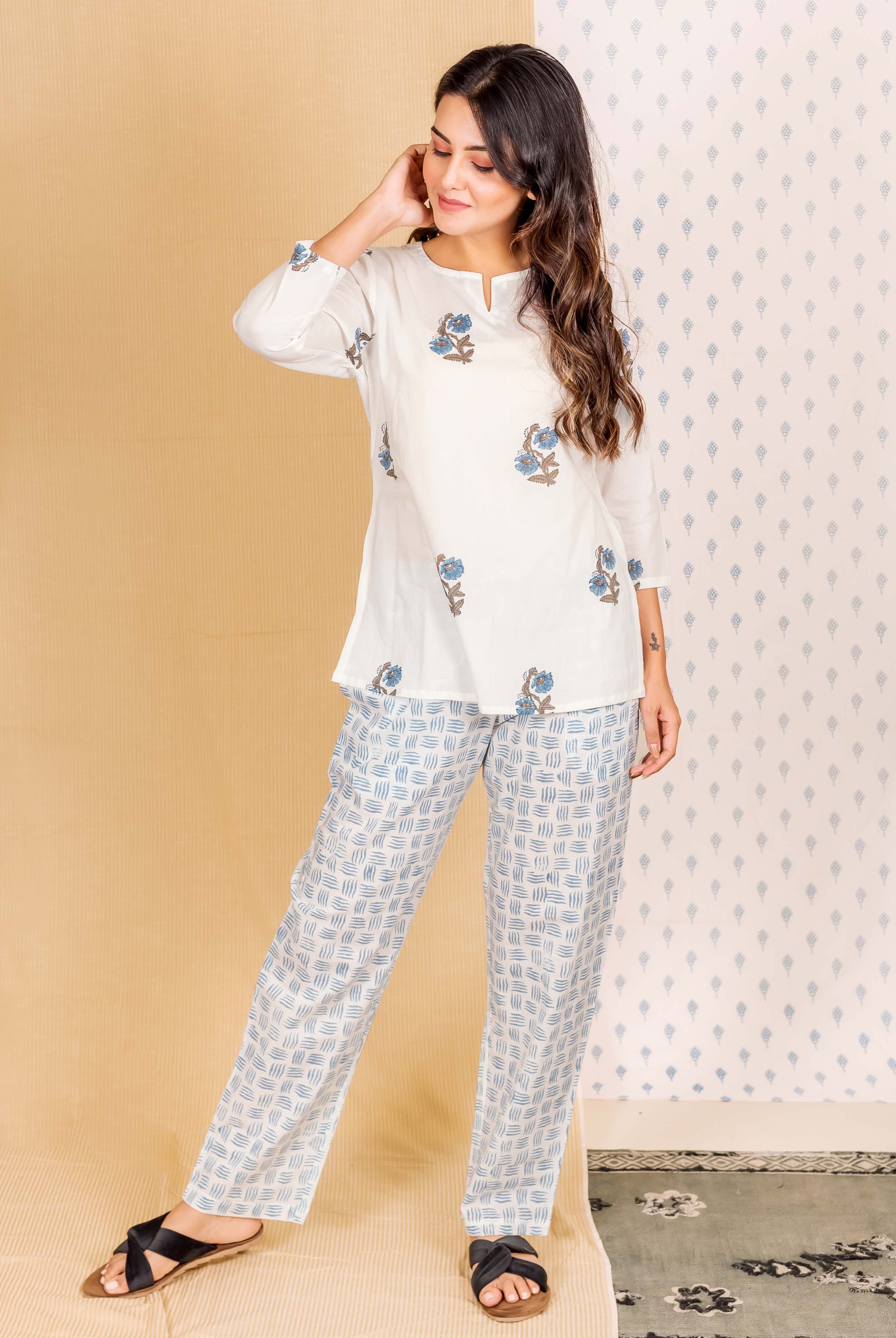 Model wears delicate white hand block printed loungewear with blue floral top and patterned pants.