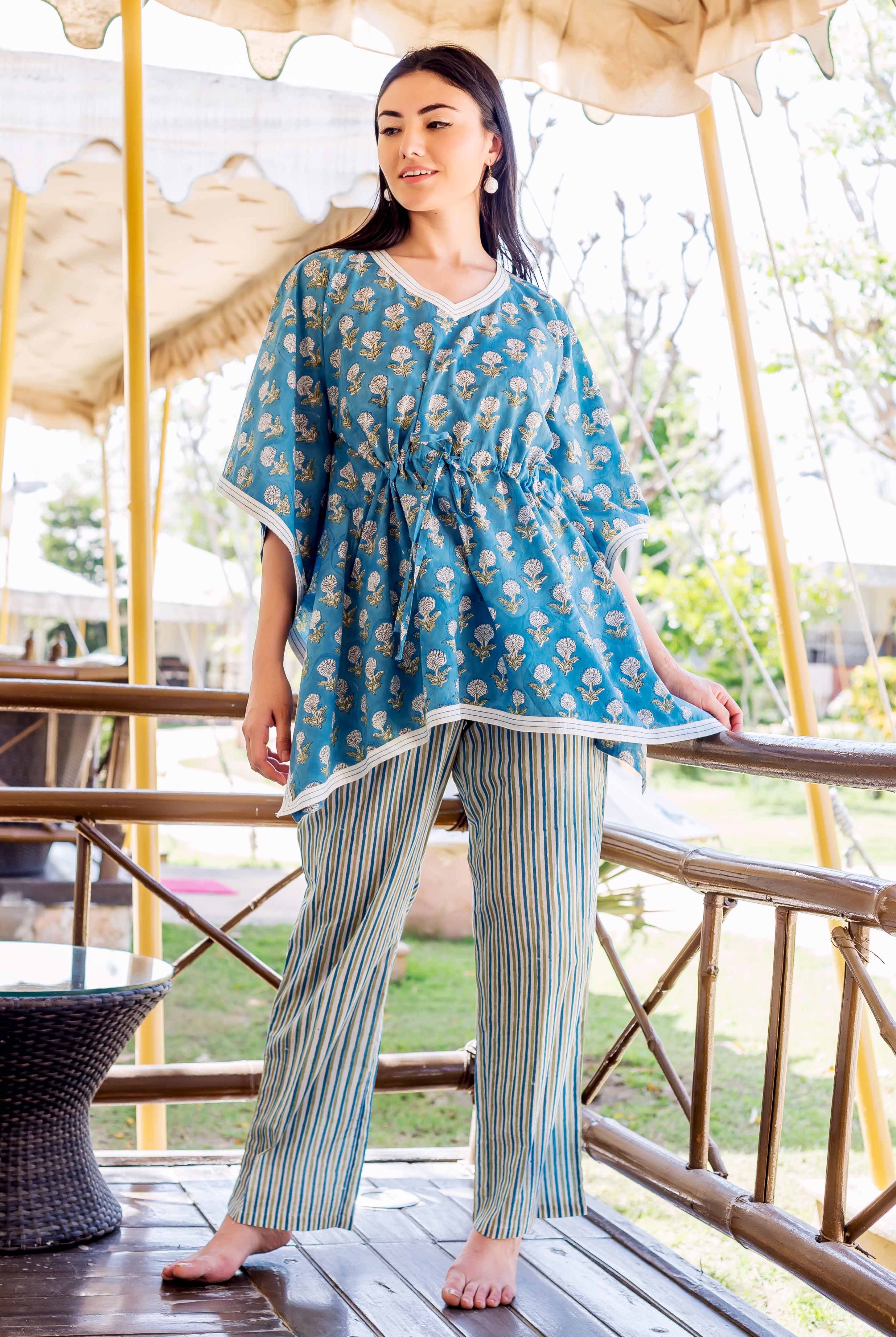 A woman wearing a blue kaftan-style top with white floral print and striped trousers.