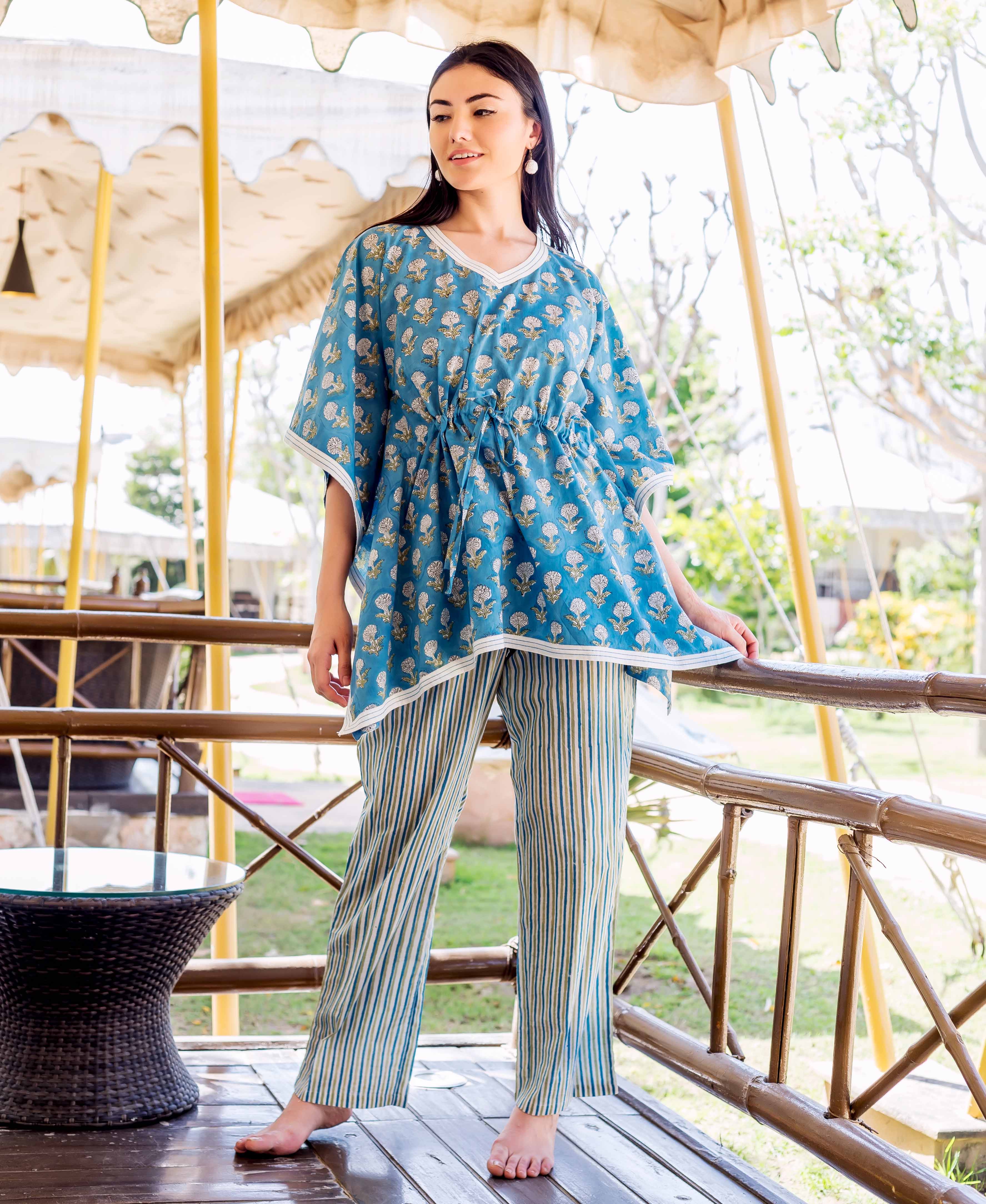 A woman wearing a blue kaftan-style top with white floral print and striped trousers.