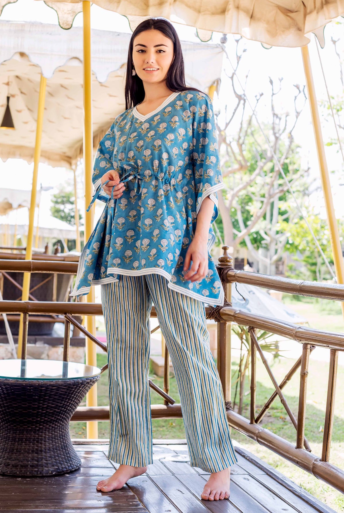 Front view of model in blue floral kaftan top with striped trousers.