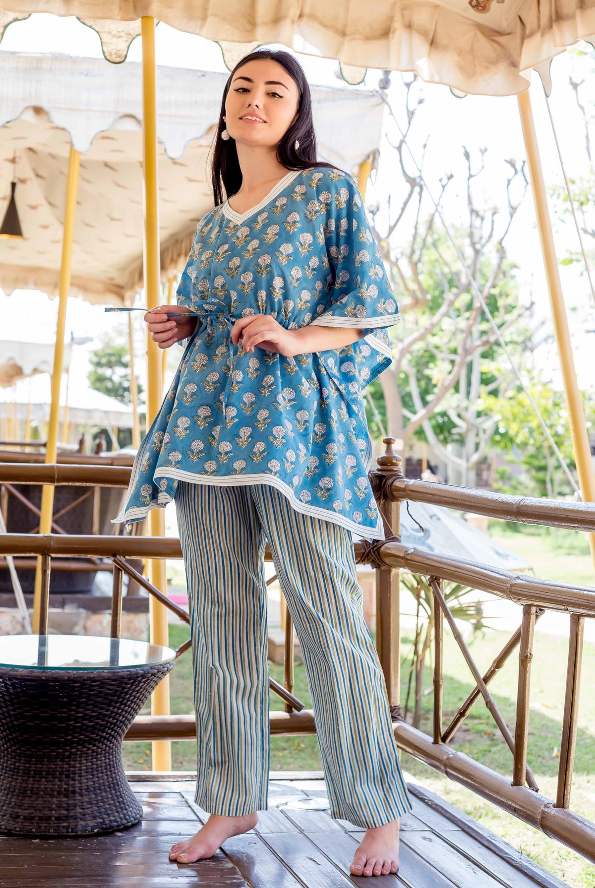 A woman wearing a blue kaftan-style top with white floral print and striped trousers.