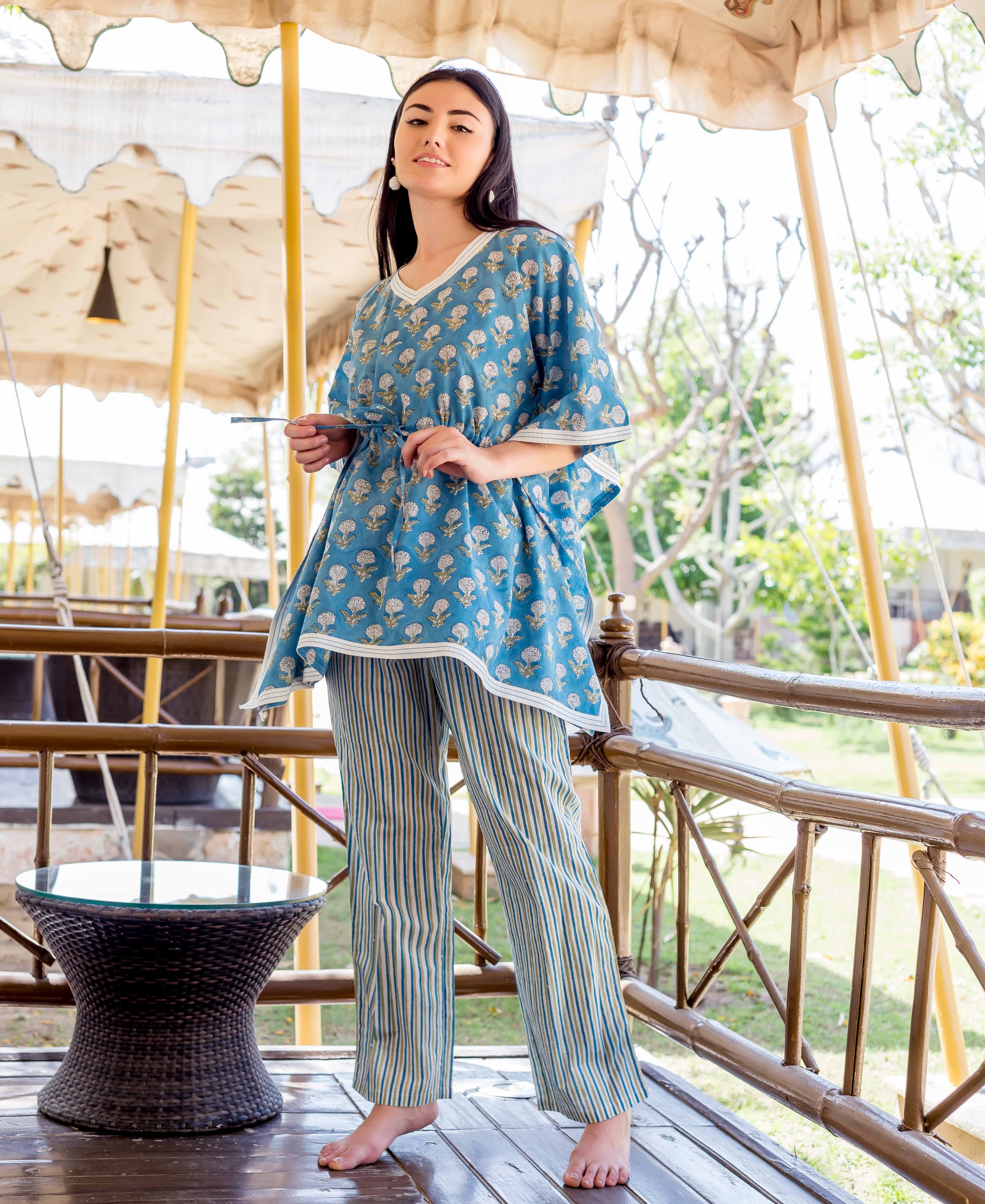 A woman wearing a blue kaftan-style top with white floral print and striped trousers.