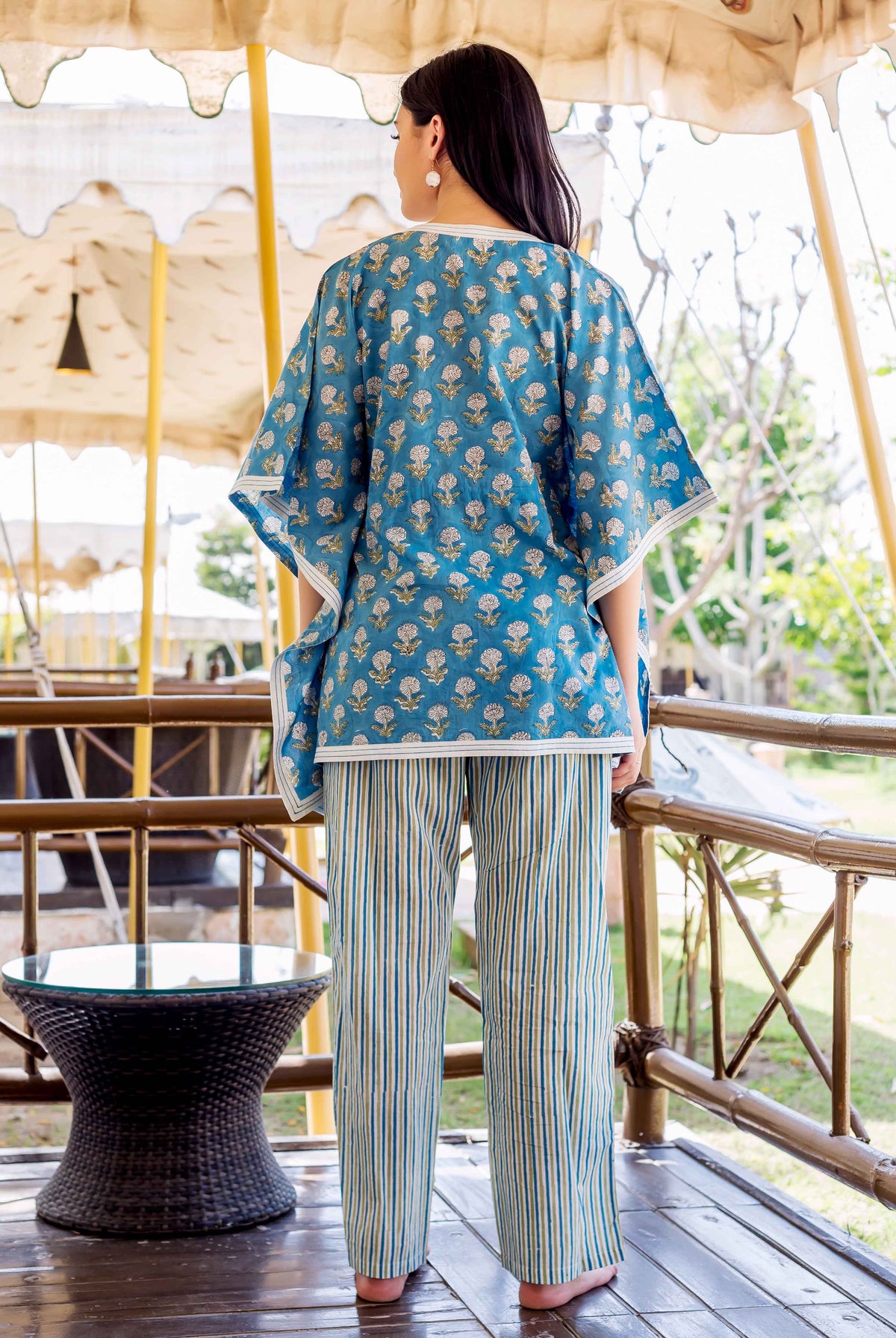A woman wearing a blue kaftan-style top with white floral print and striped trousers.