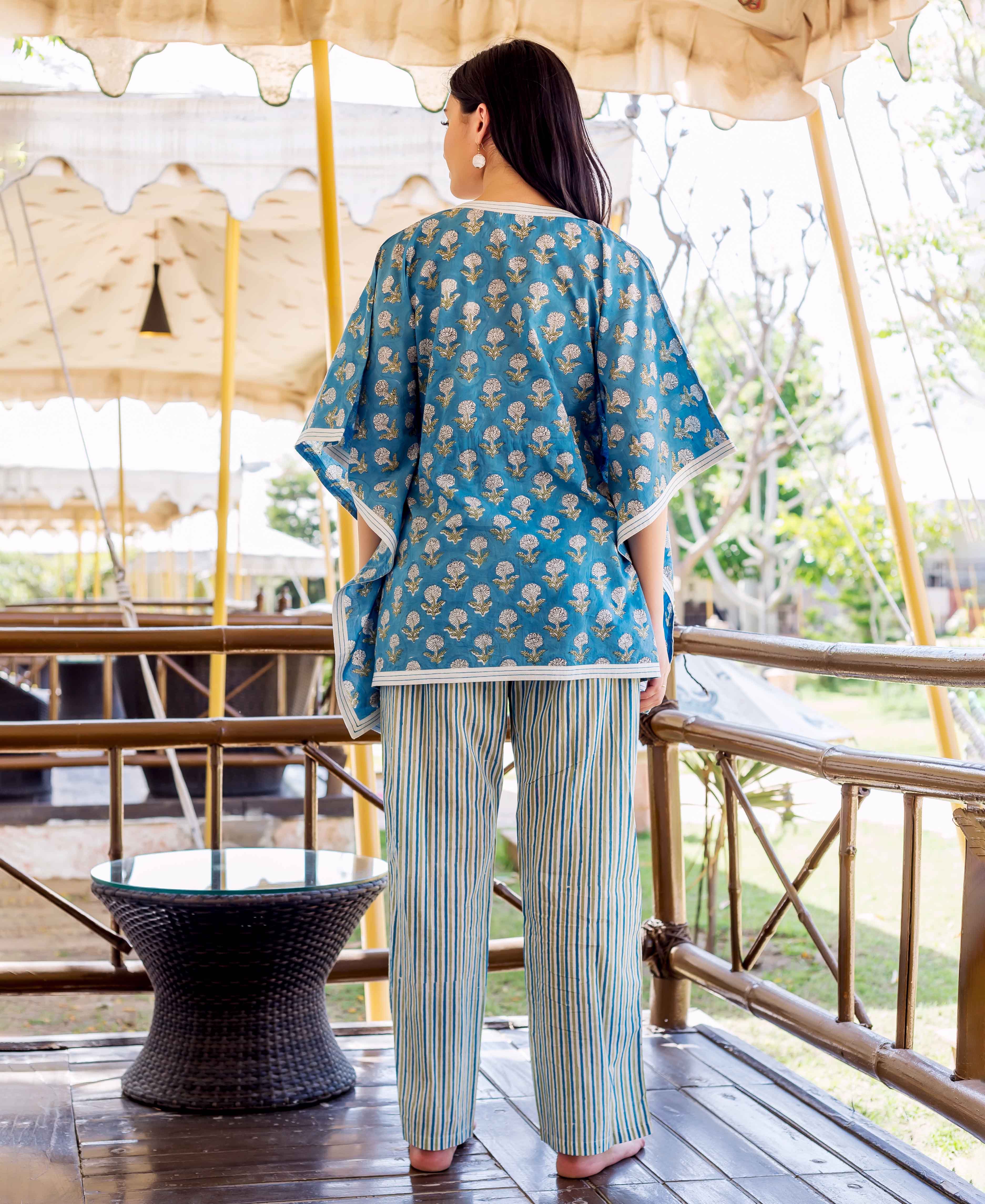 A woman wearing a blue kaftan-style top with white floral print and striped trousers.
