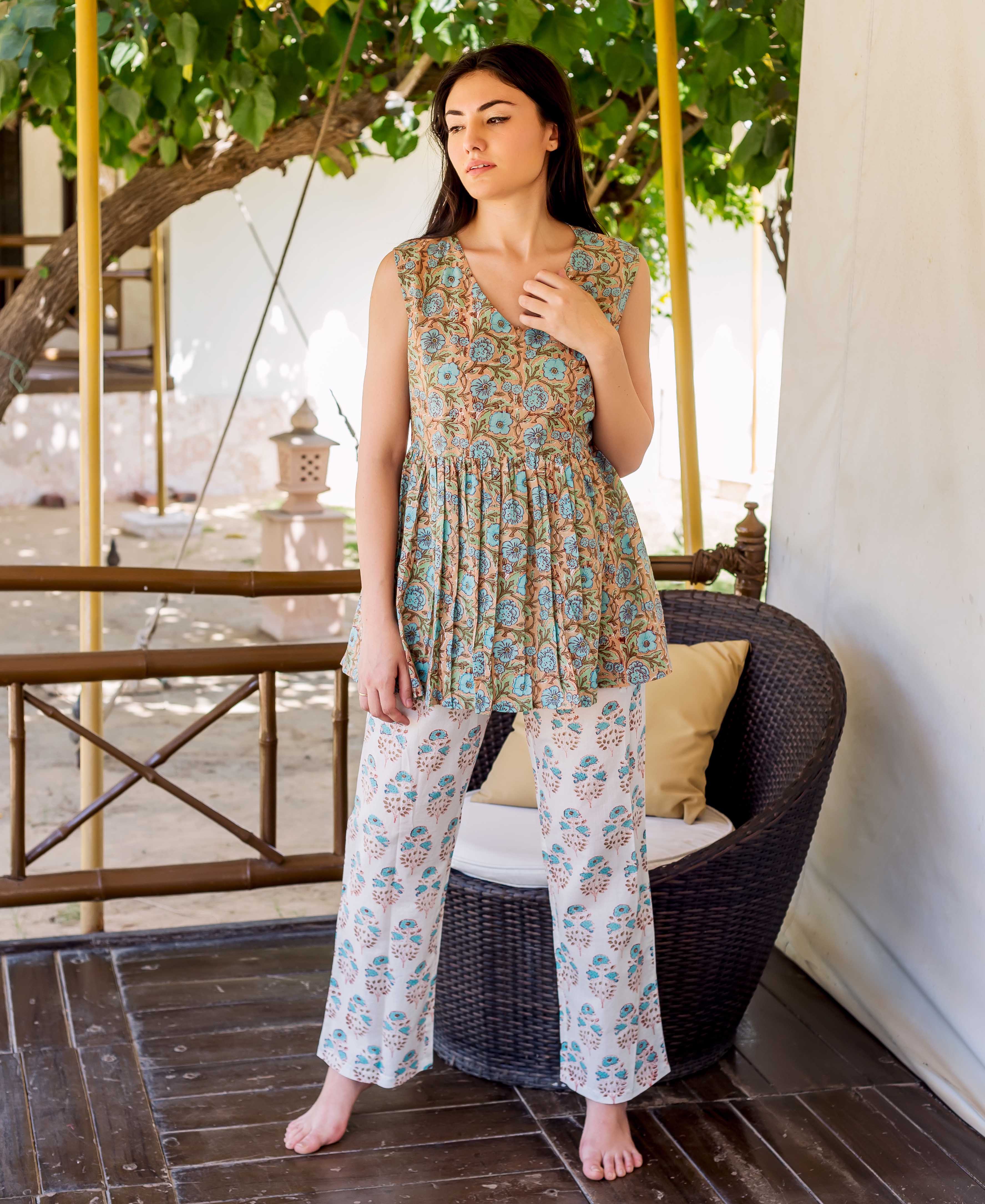 Model in full-length wearing a beige peplum top and white pants with blue block print.