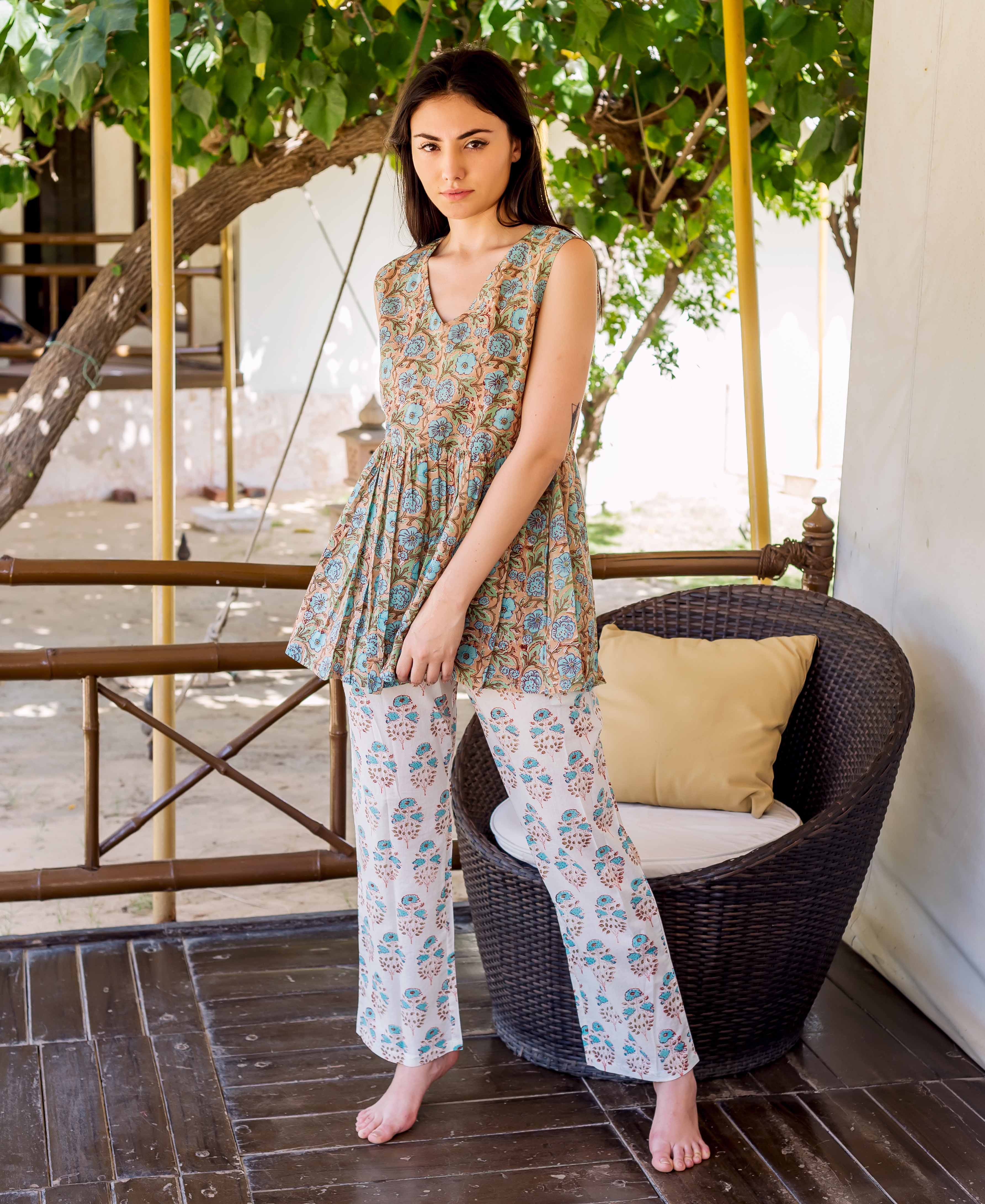 Model in a sleeveless brown and teal floral hand block printed peplum top and white pants.