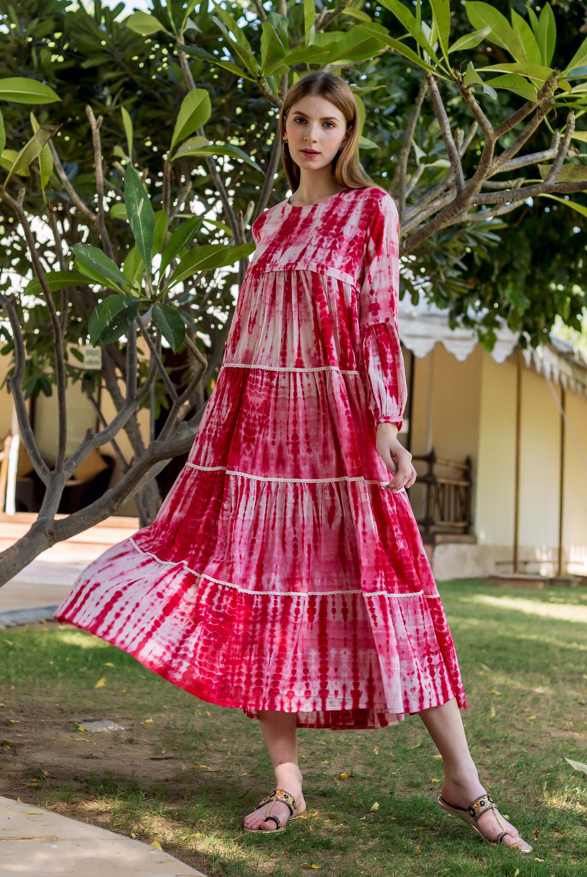 Model wearing a full-length red and white tie-dye tiered dress with long sleeves.