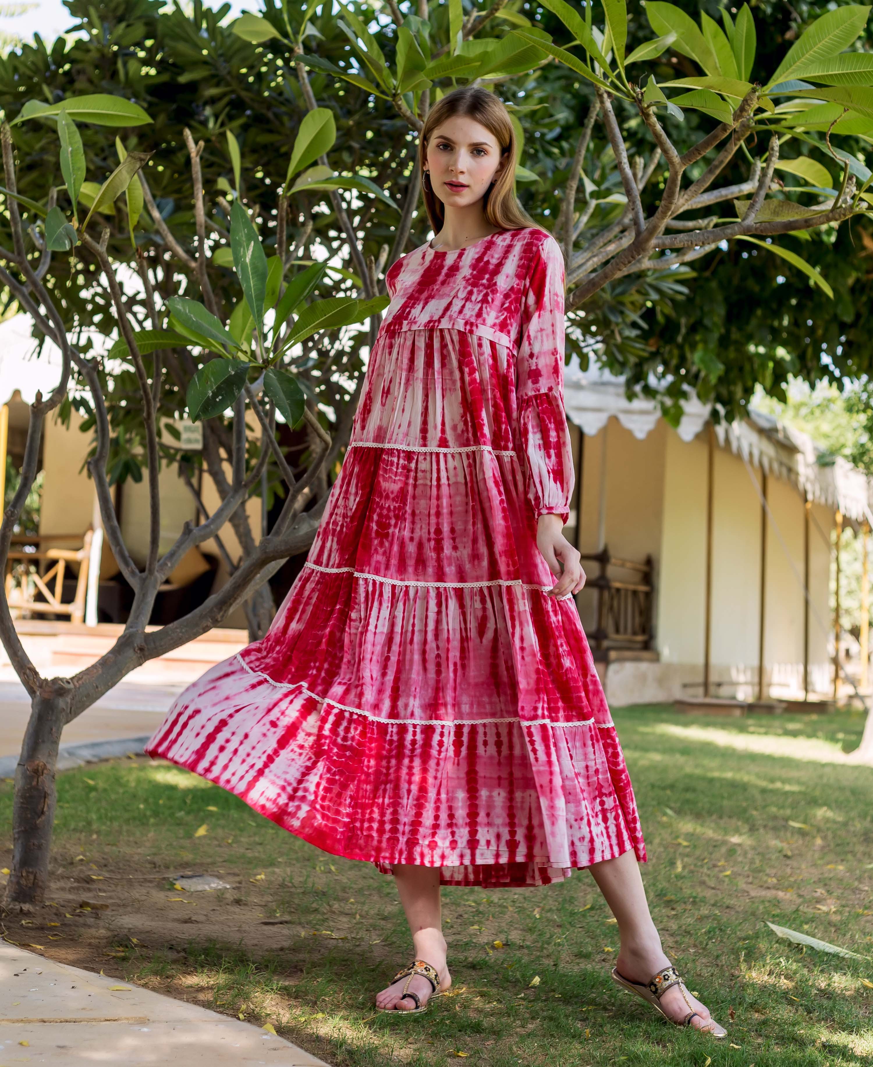 Model wearing a full-length red and white tie-dye tiered dress with long sleeves.