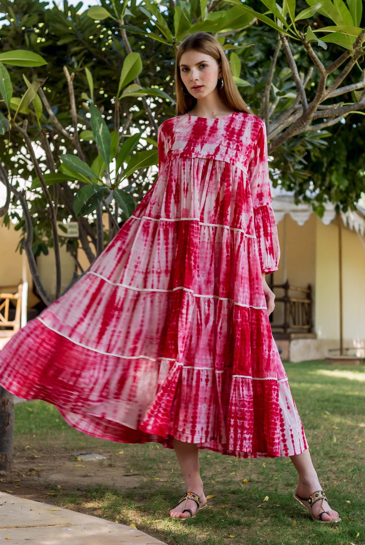 Full-body shot of a model wearing a vibrant red tie-dye tiered dress outdoors.