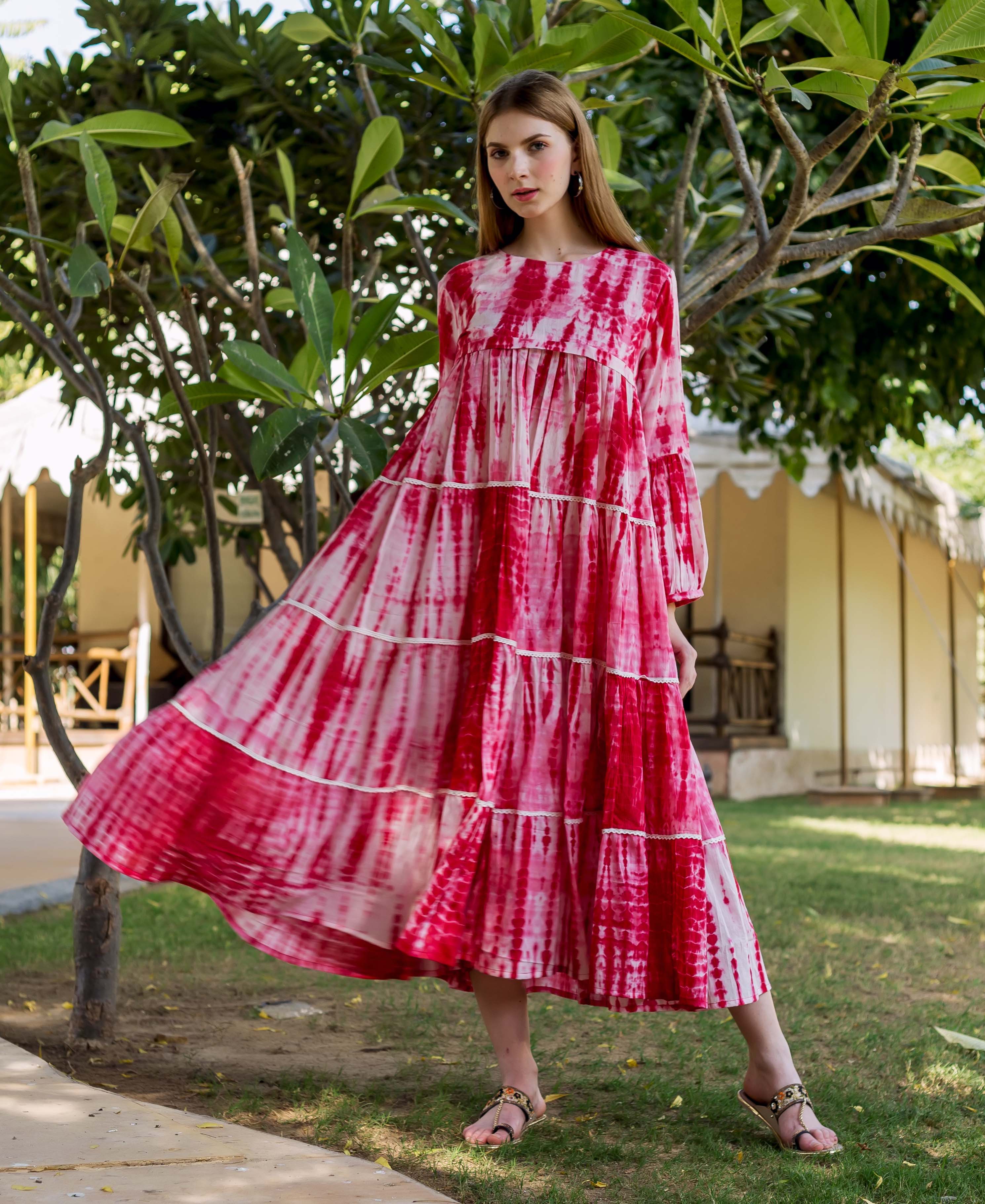 Full-body shot of a model wearing a vibrant red tie-dye tiered dress outdoors.
