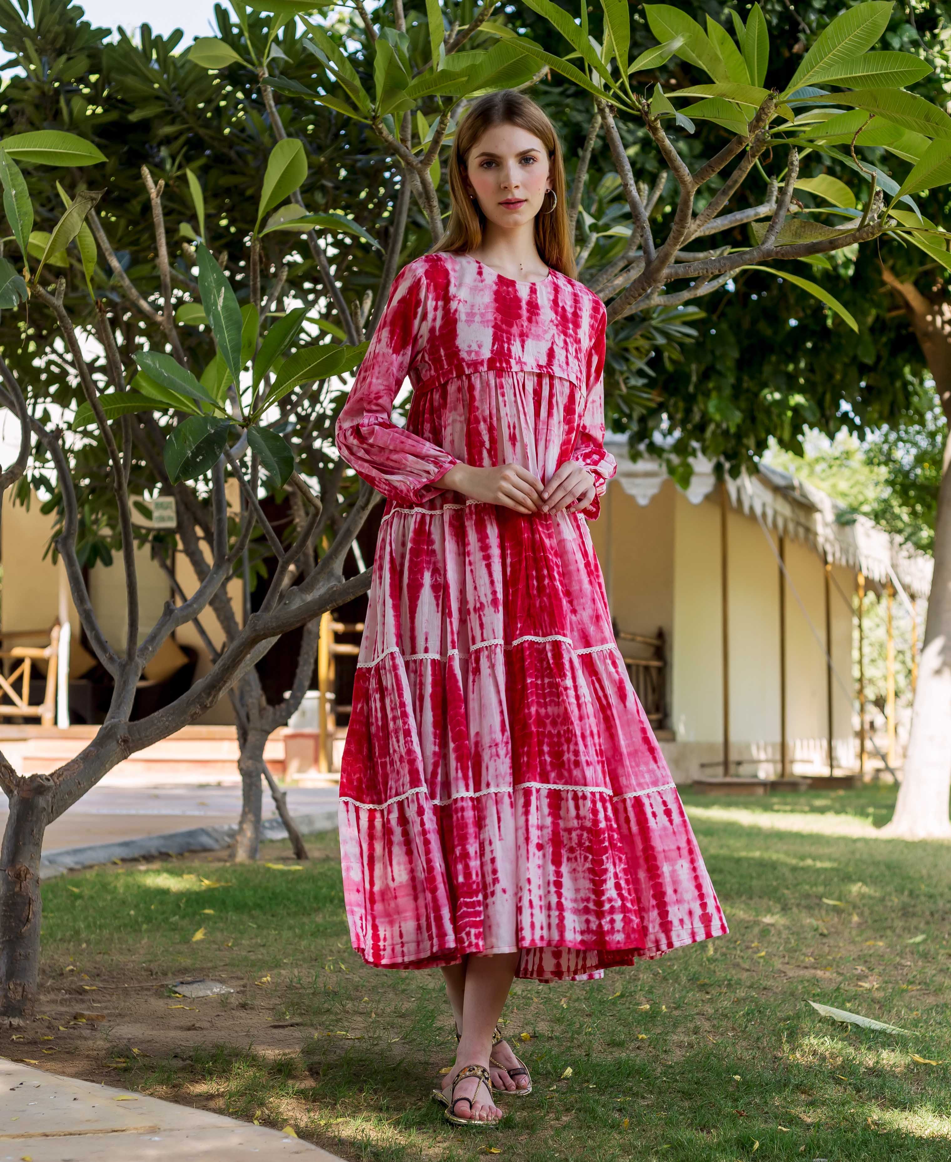 Woman in a vibrant red tie-dye tiered dress with long sleeves, standing in a garden.