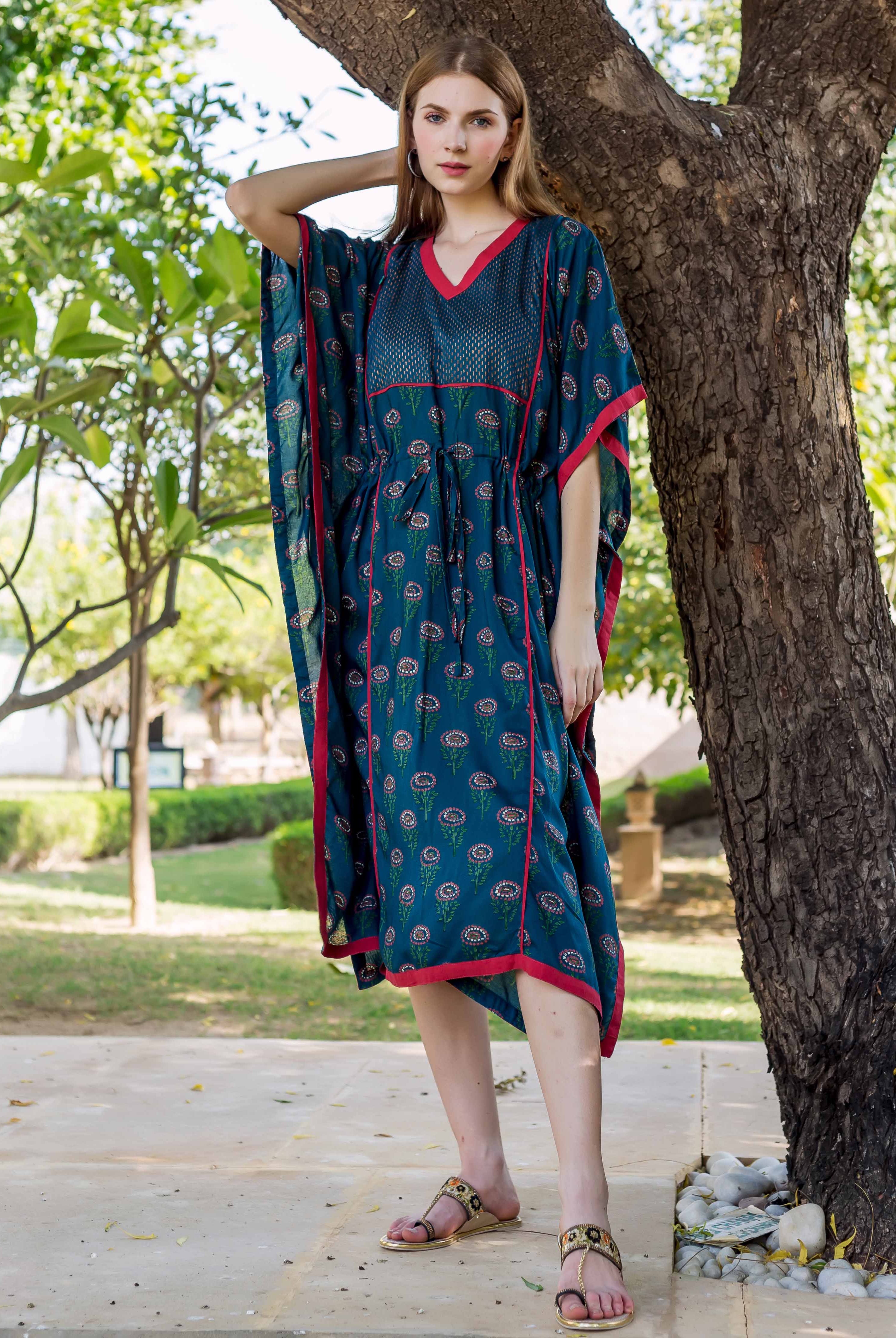 Model wearing peacock green hand-block-printed kaftan with red trim, standing by a tree.