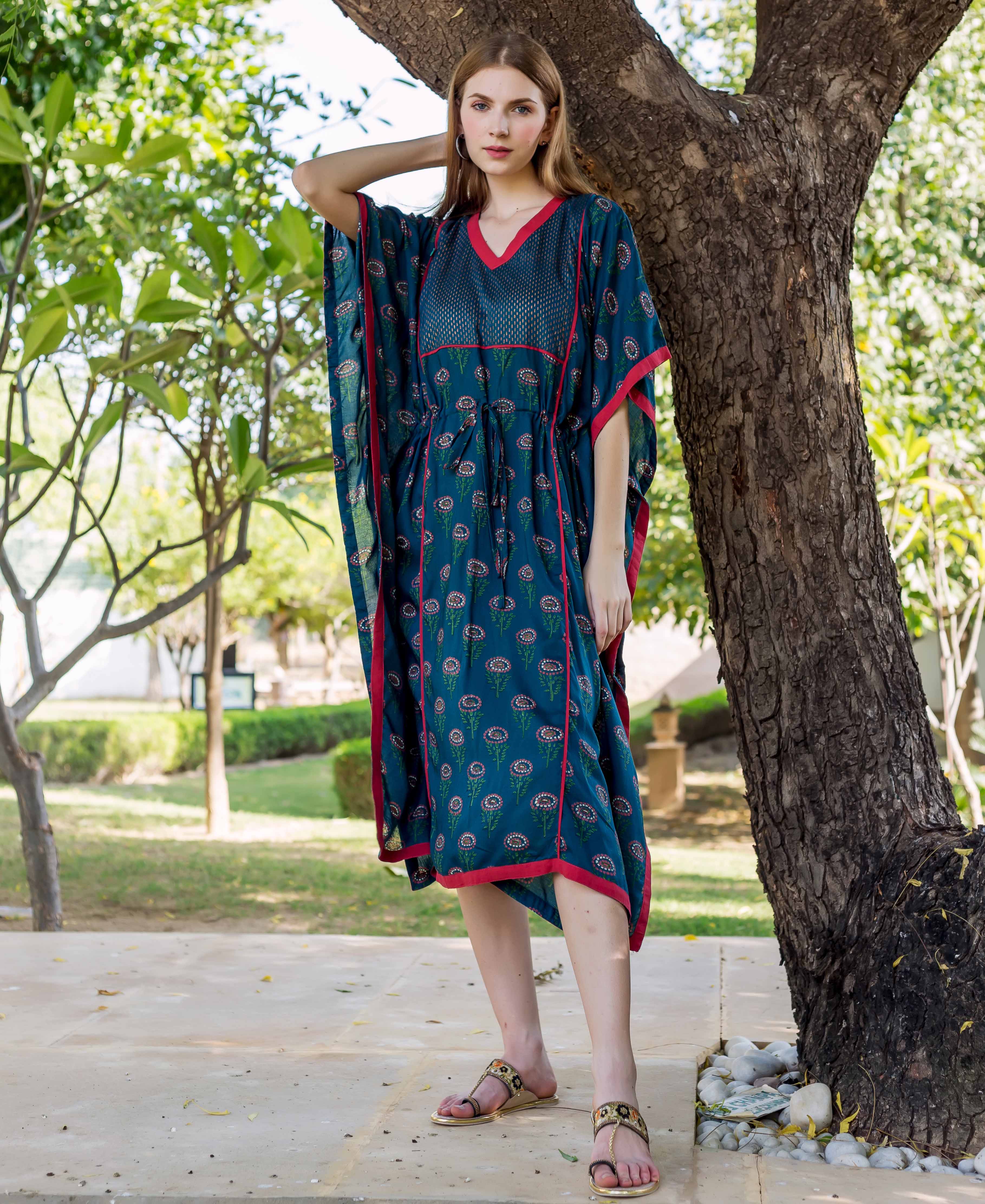 Model wearing peacock green hand-block-printed kaftan with red trim, standing by a tree.