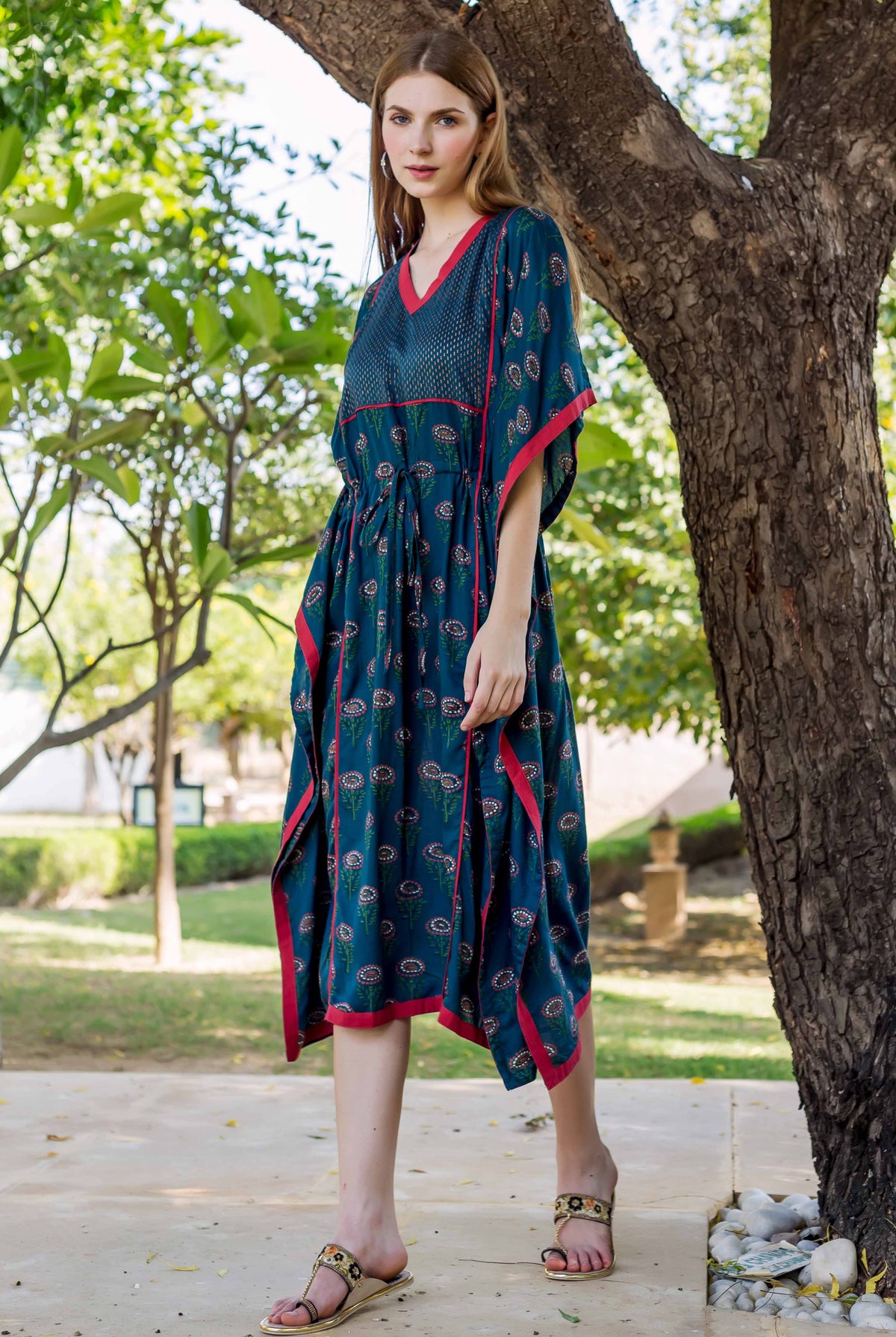 Standing model wearing a peacock green hand-block-printed kaftan with red trim and floral print.