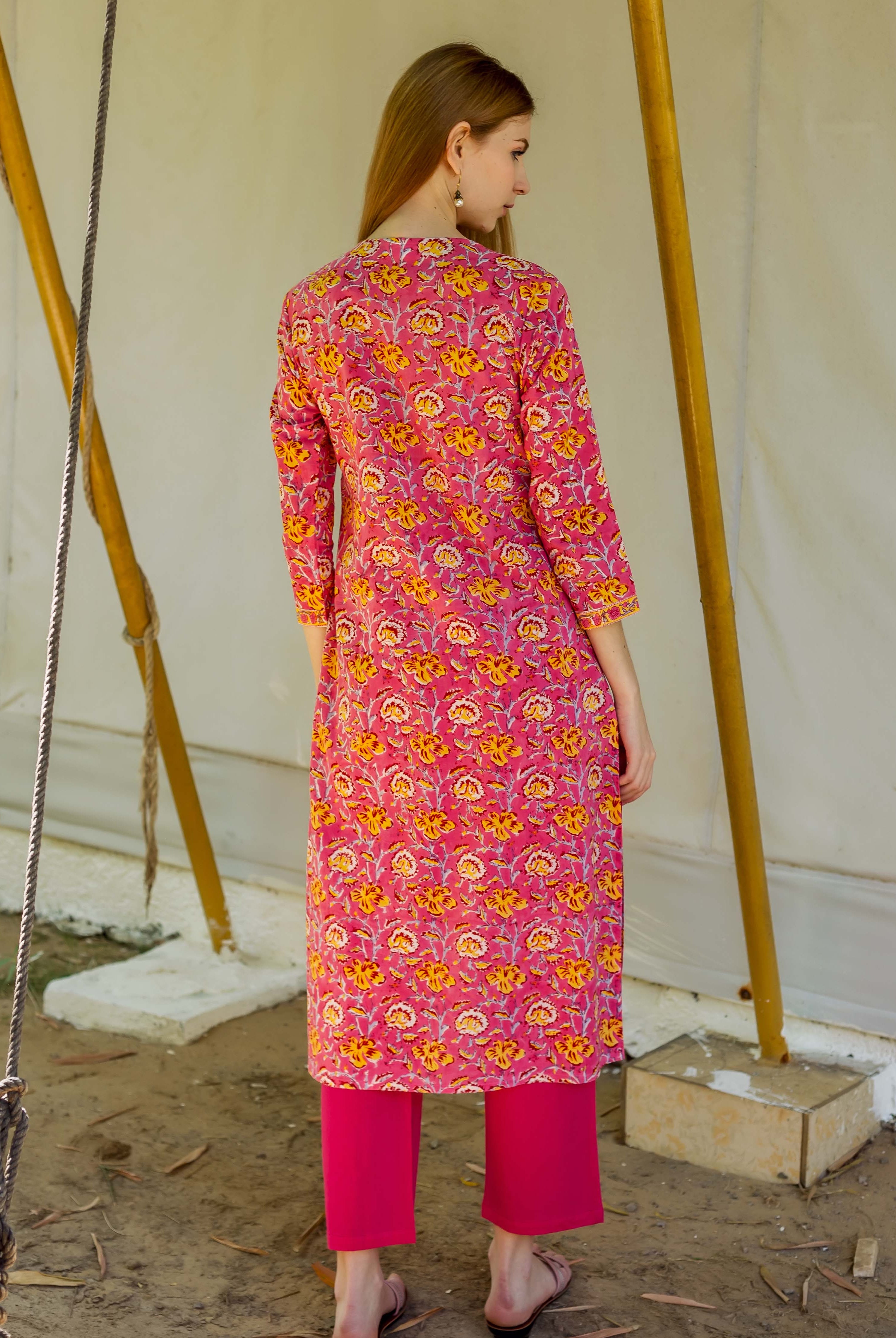 Back view of a woman wearing a pink floral hand-block printed kurta and magenta pants.