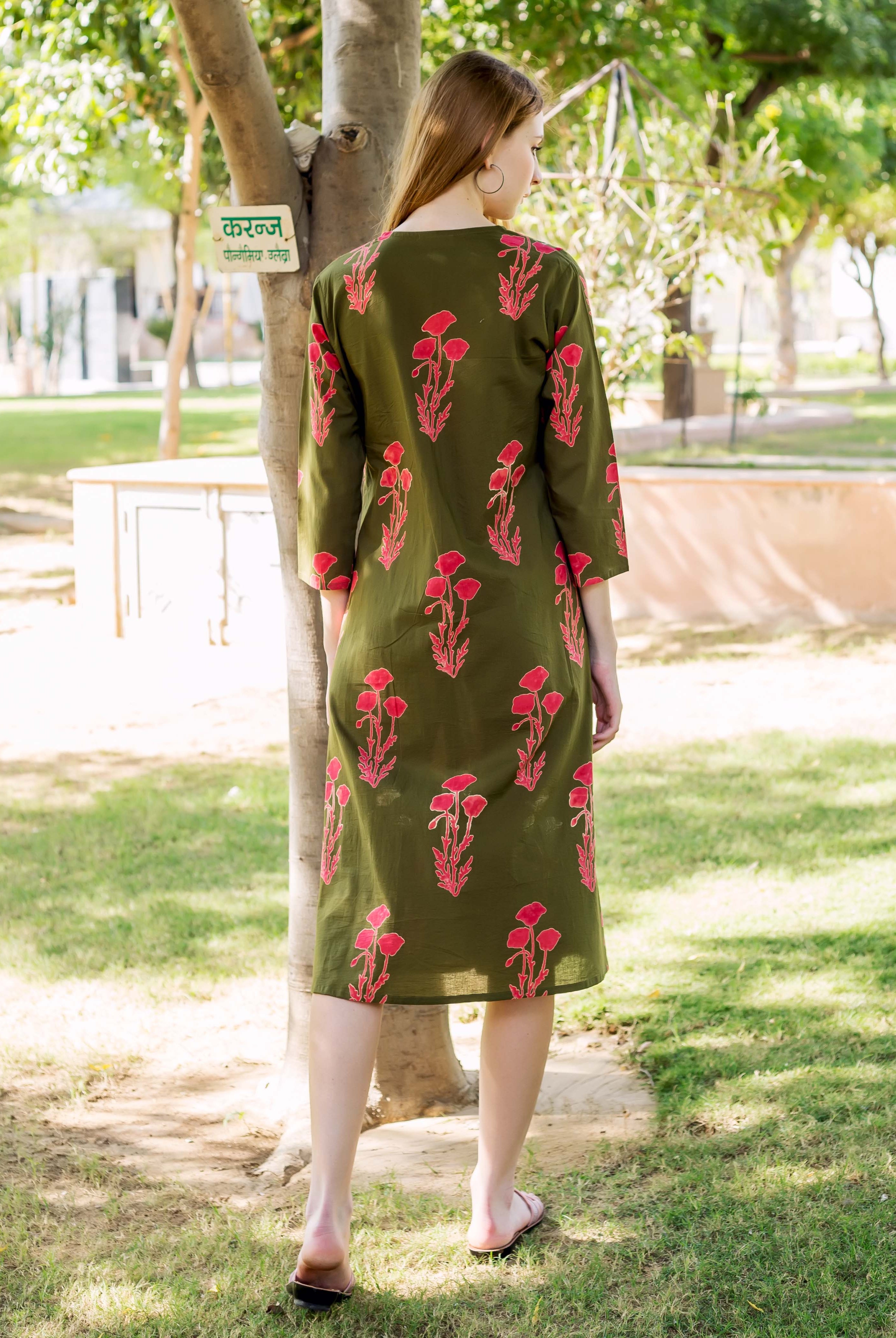 A woman wearing an olive green dress with pink floral print, standing outdoors.