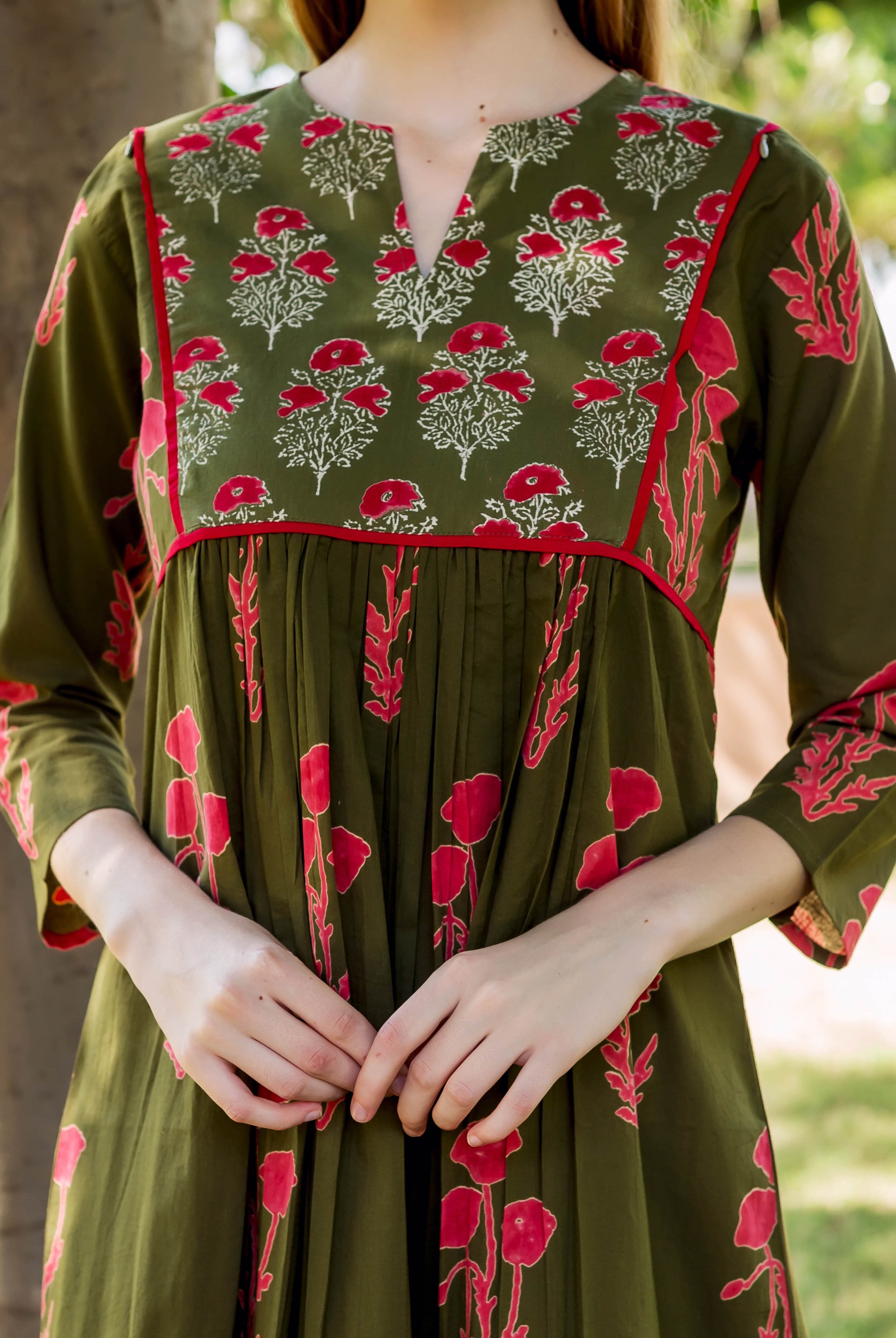 Olive green hand-block printed dress with red-white floral yoke and gathered body on a model.
