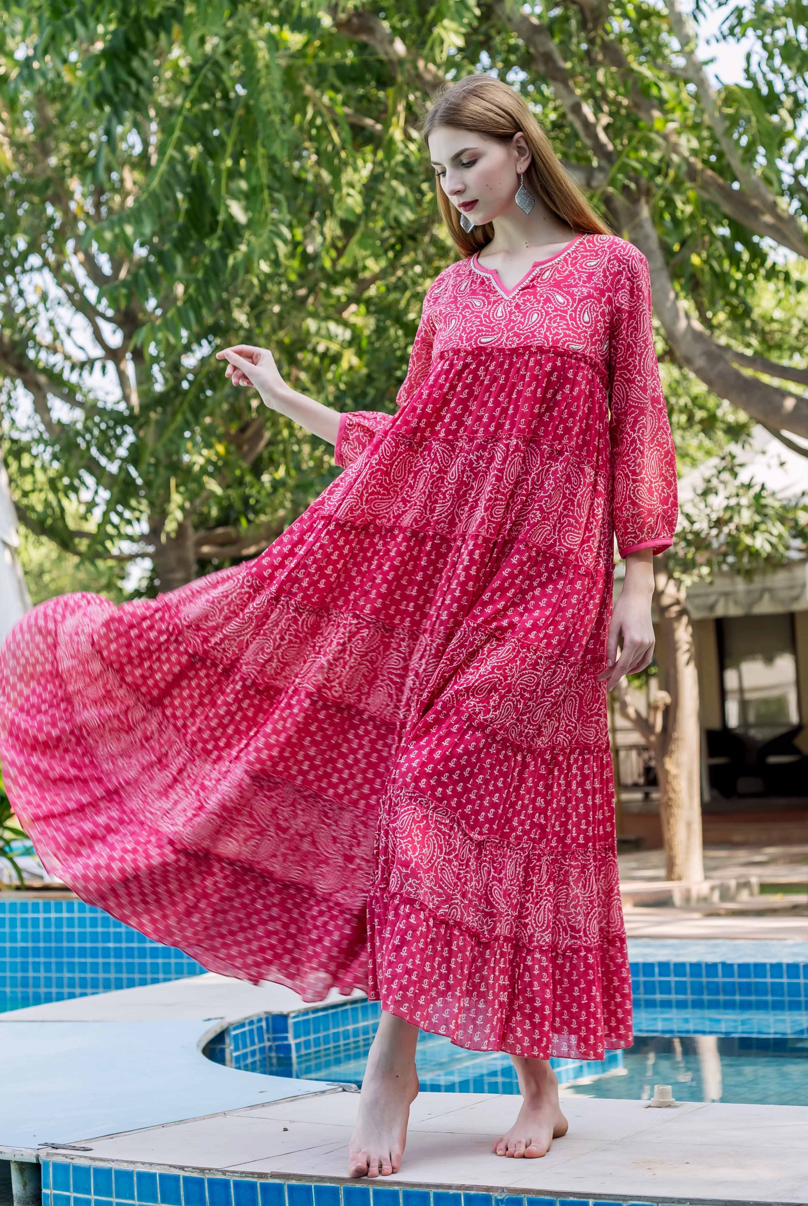 Model in a flowing fuchsia tiered dress with light hand-block-print standing by a pool.