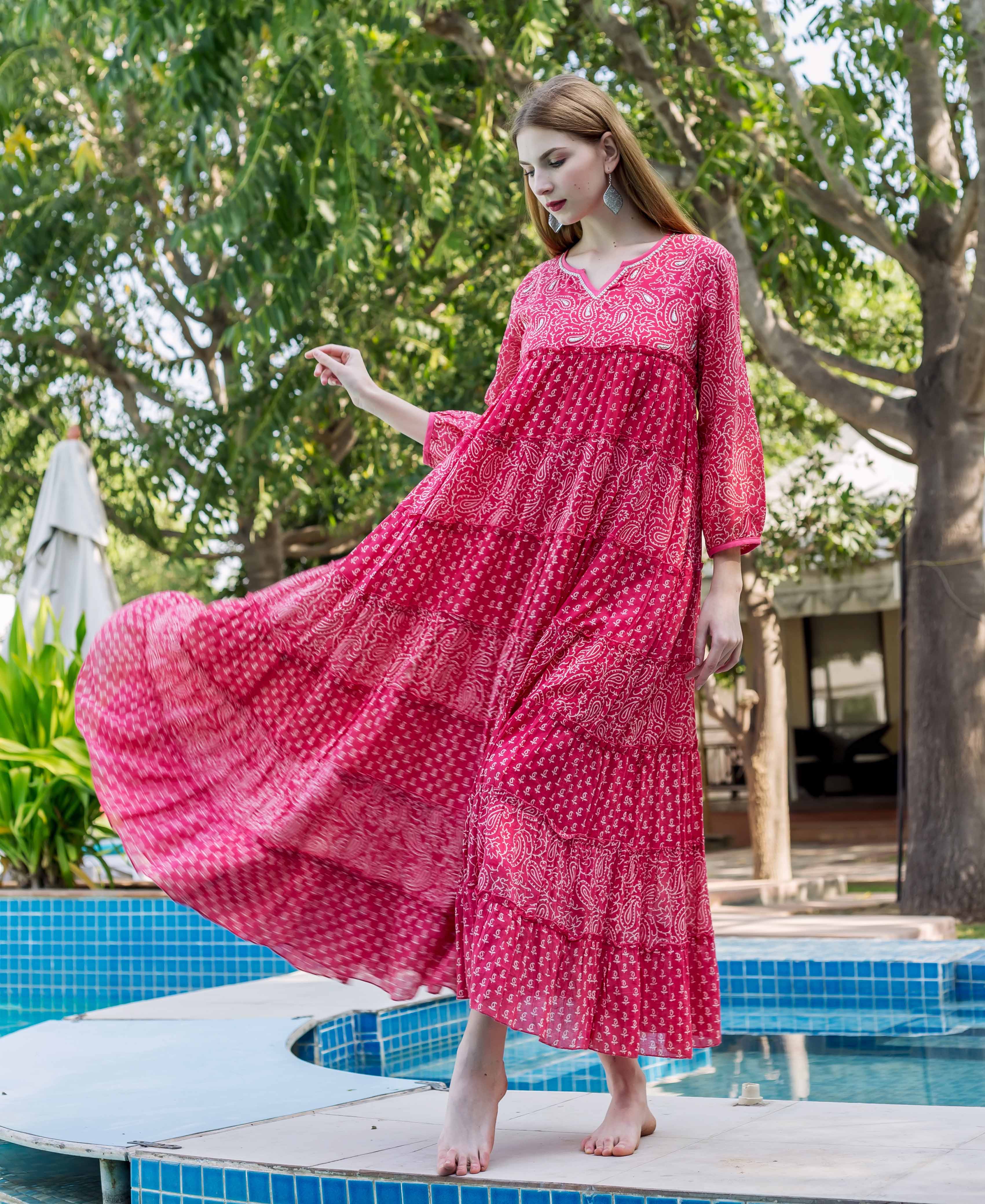 Model in a flowing fuchsia tiered dress with light hand-block-print standing by a pool.