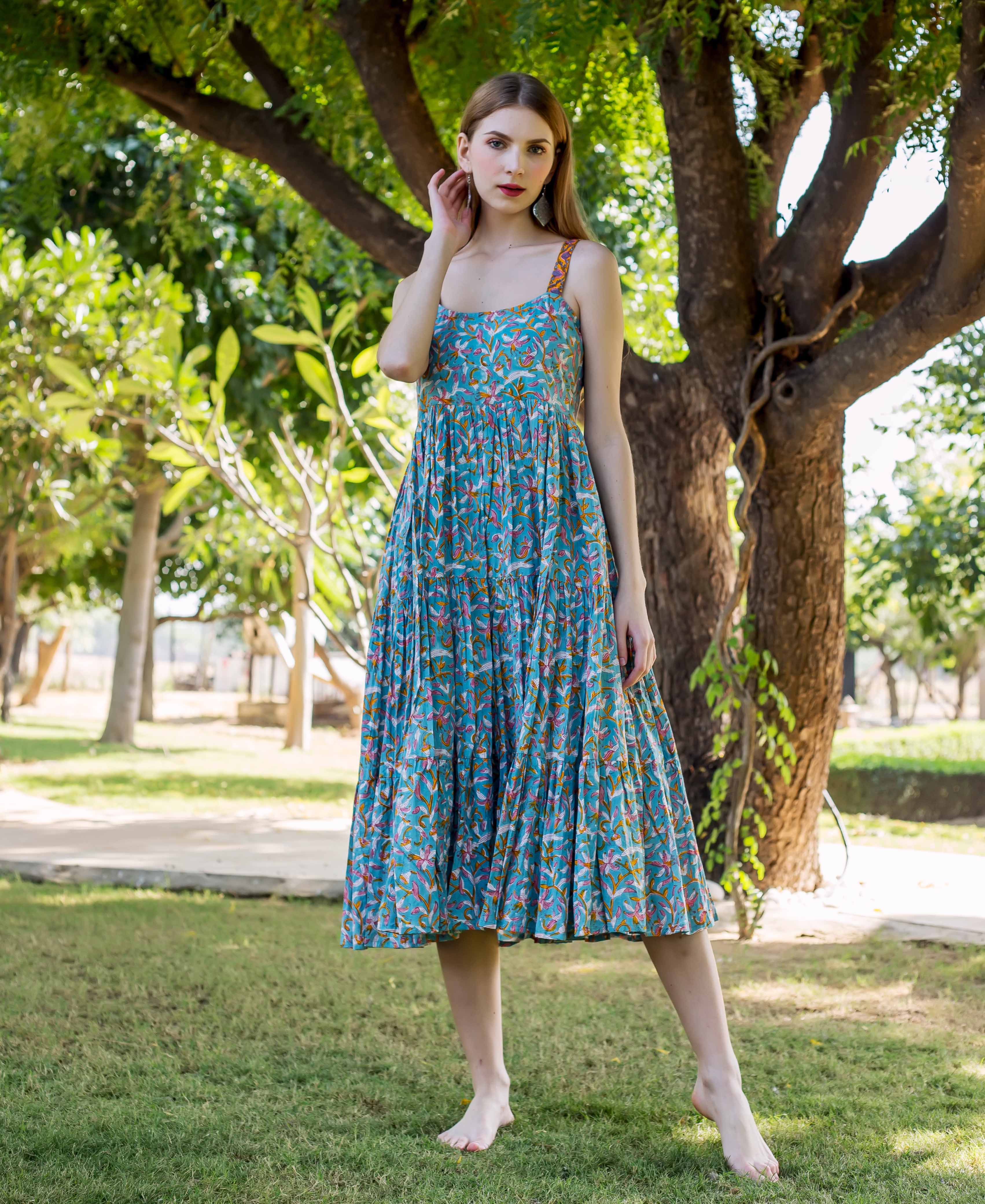 Full-length model in a strappy blue hand-block-printed floral tiered midi dress outdoors.