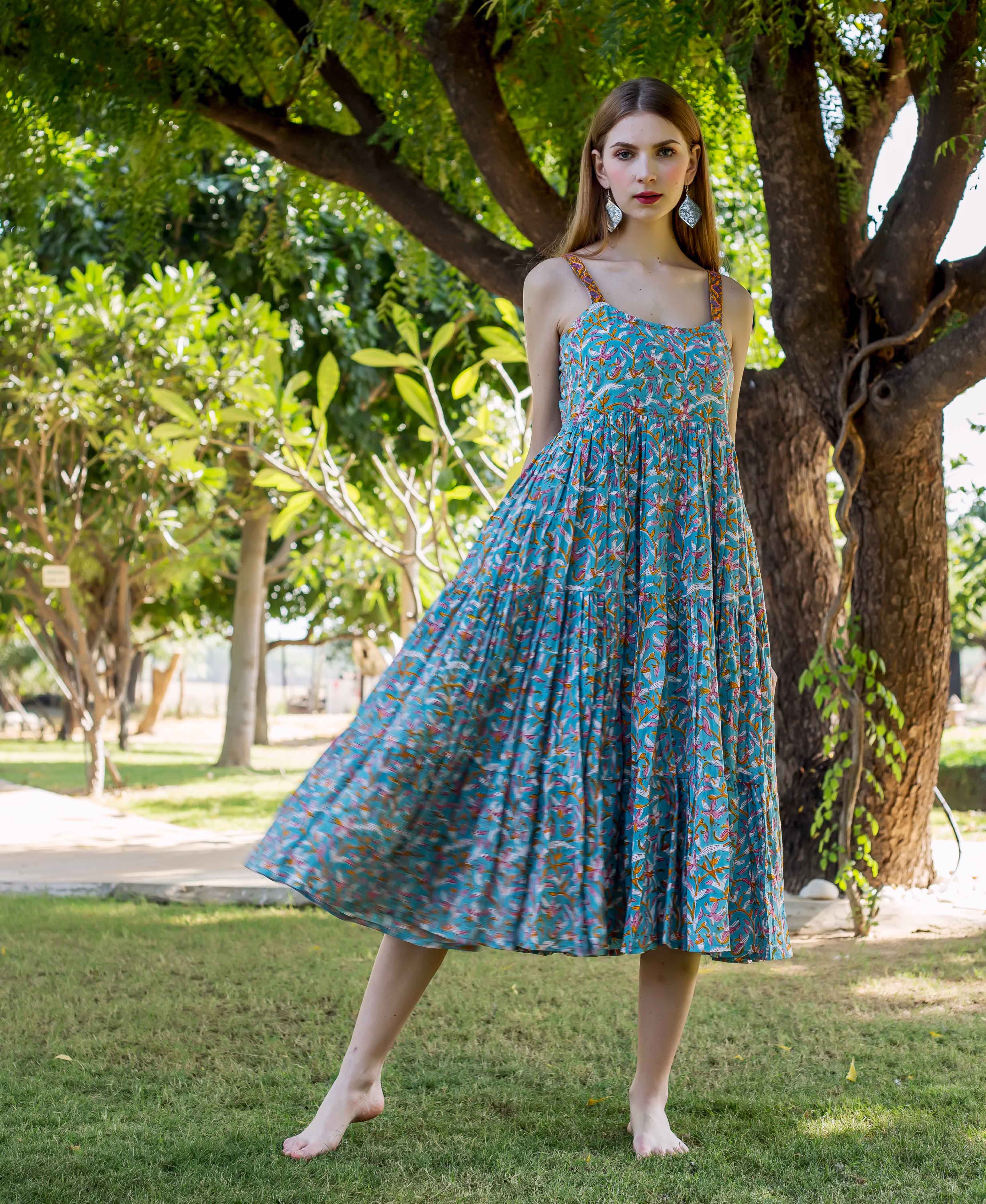 Model wears a flowing blue tiered hand-block printed dress with colorful floral and bird patterns.