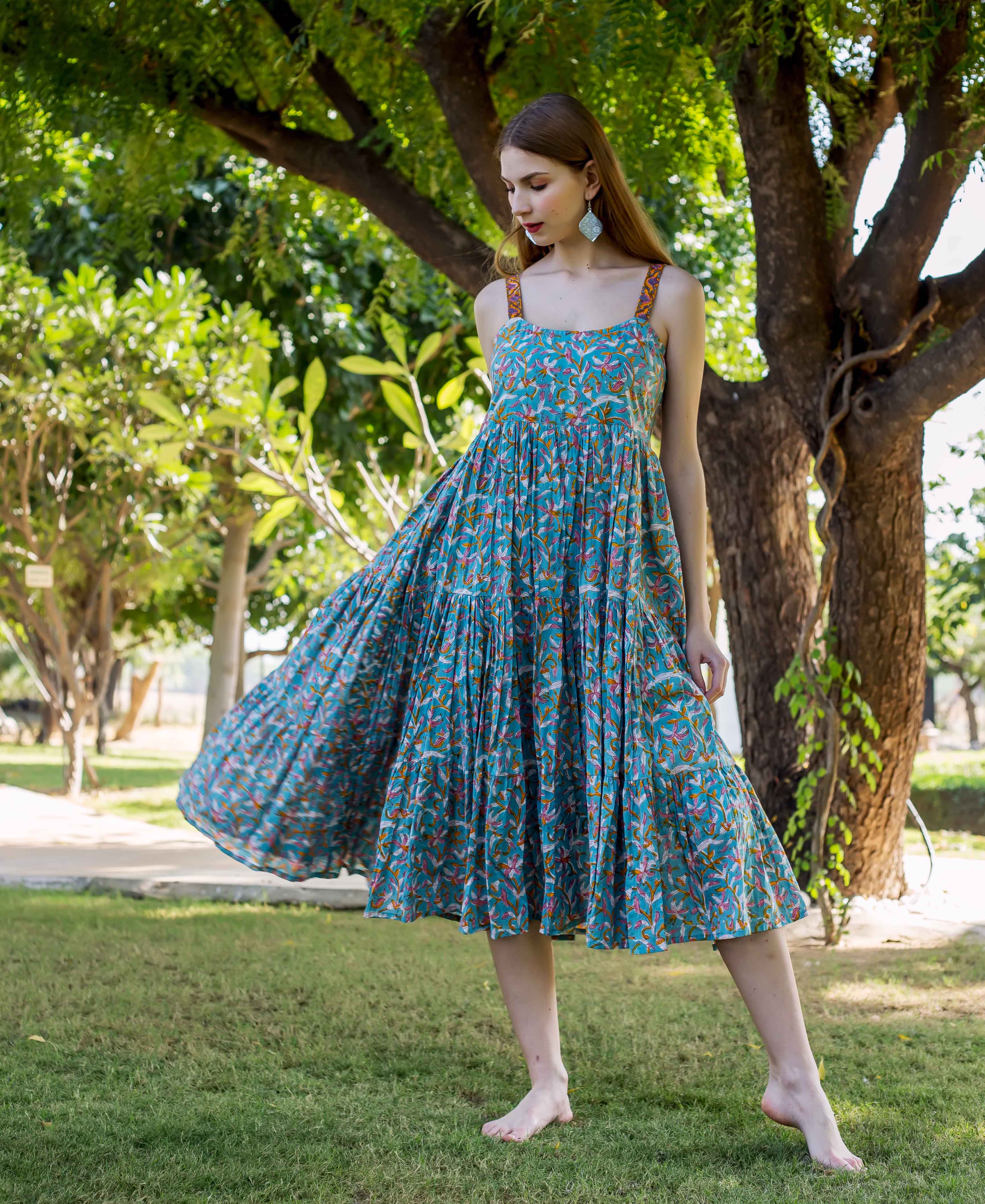 Model wearing a full-length teal blue tiered dress with a lively floral and bird print.