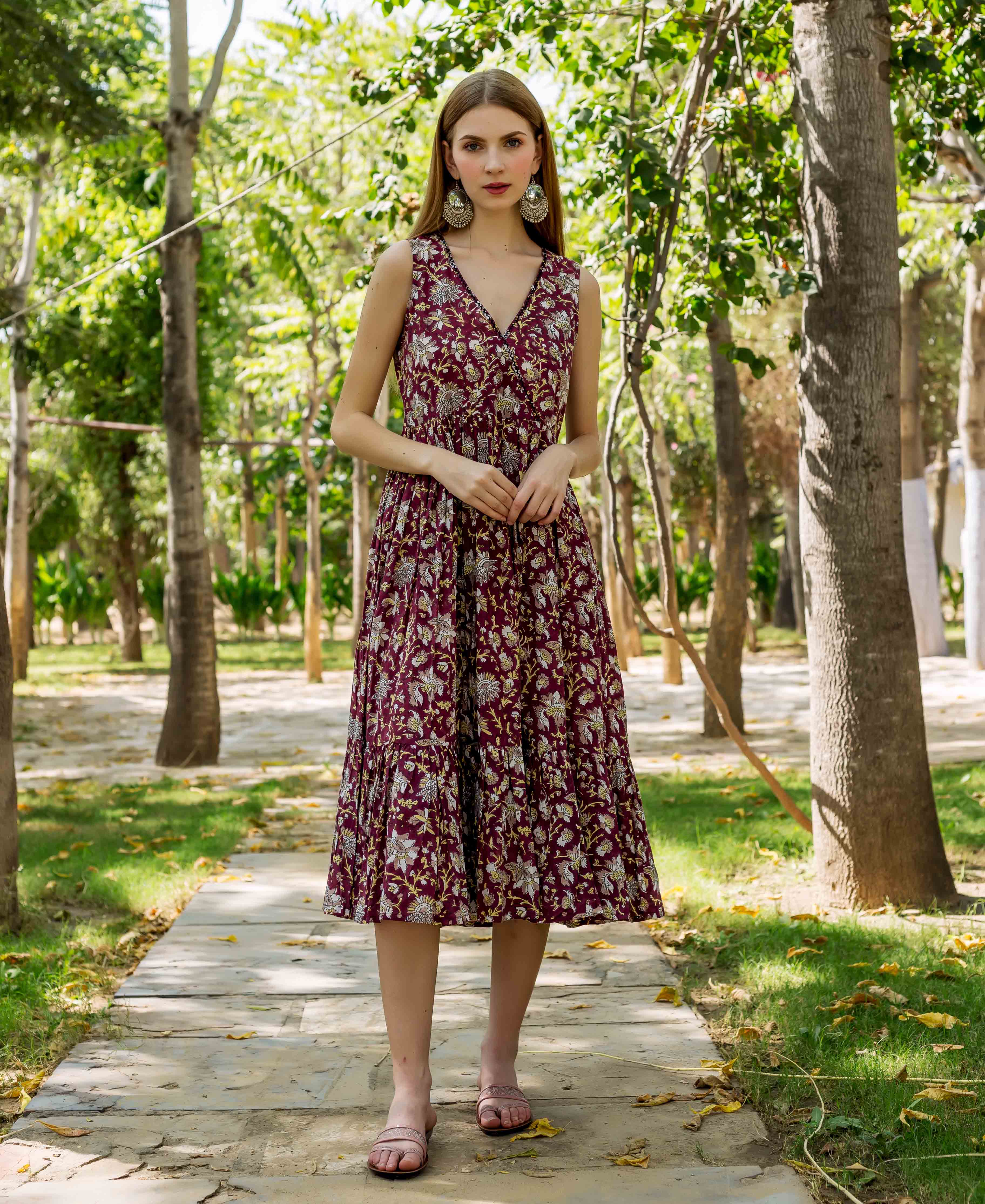 Front view model in maroon hand-block-printed floral sleeveless V-neck tiered midi dress.