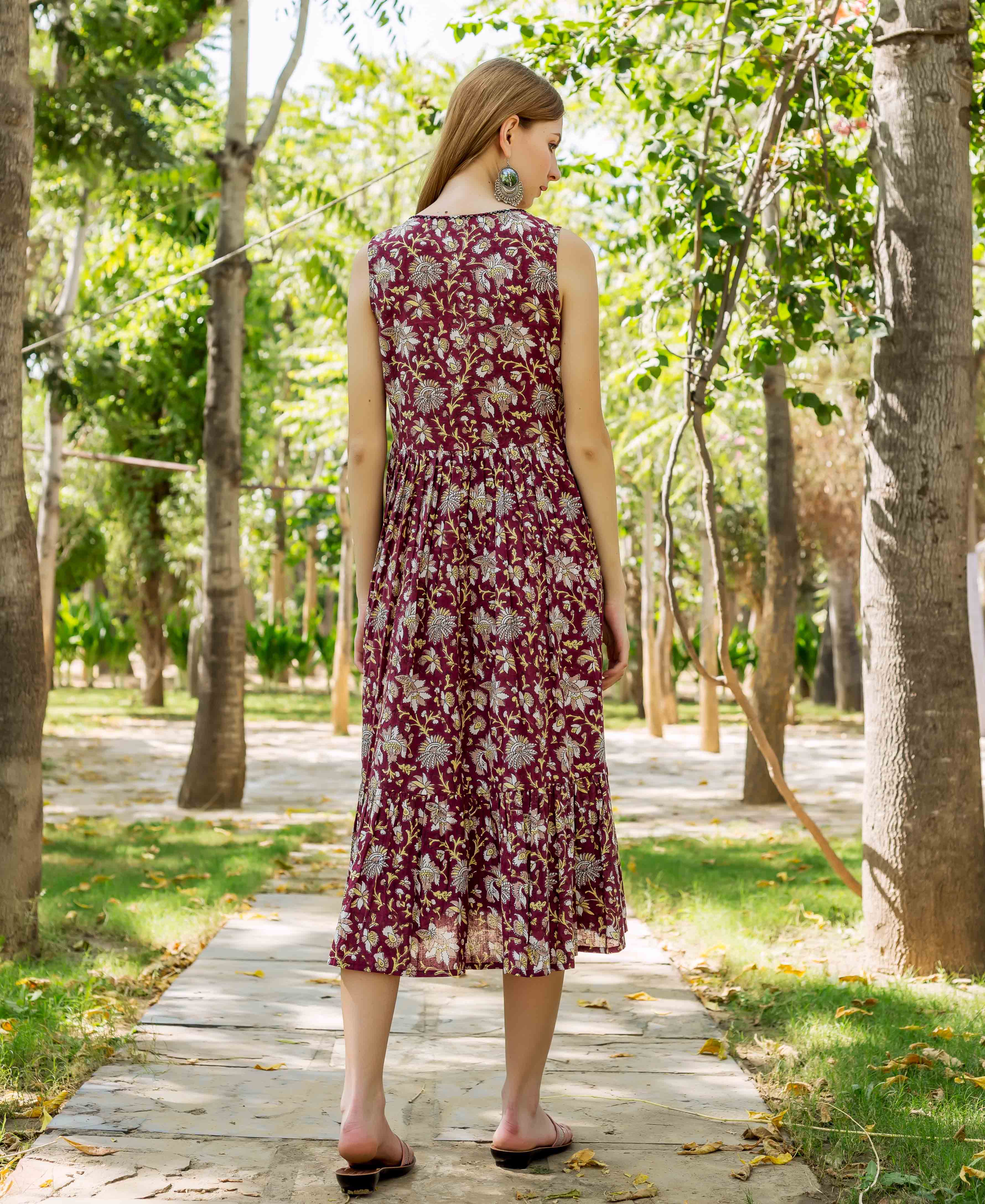 Model's back in a sleeveless maroon printed tiered dress with white and gold floral pattern.