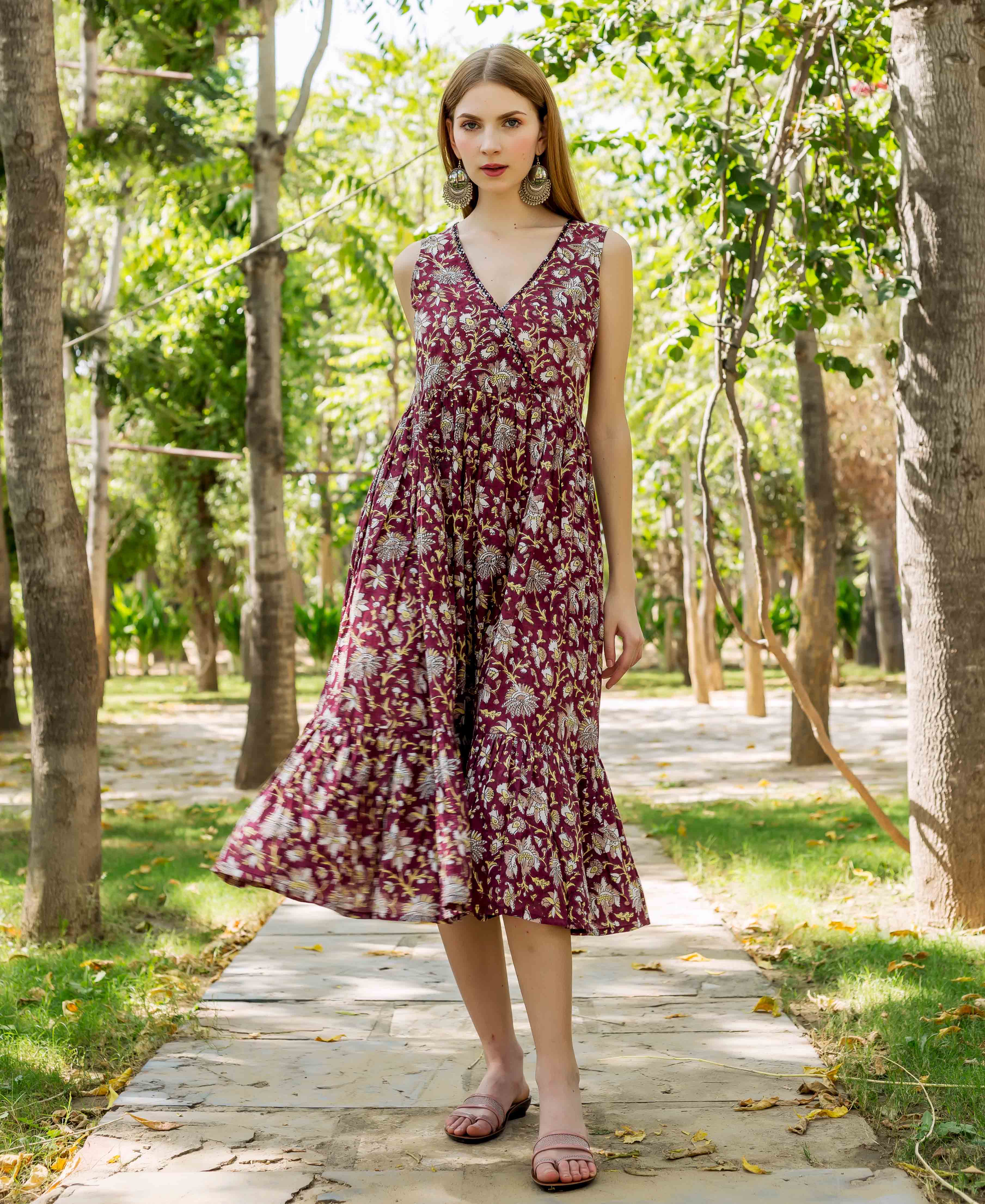 Model wears a deep burgundy floral hand-block printed sleeveless tiered dress, skirt flowing.