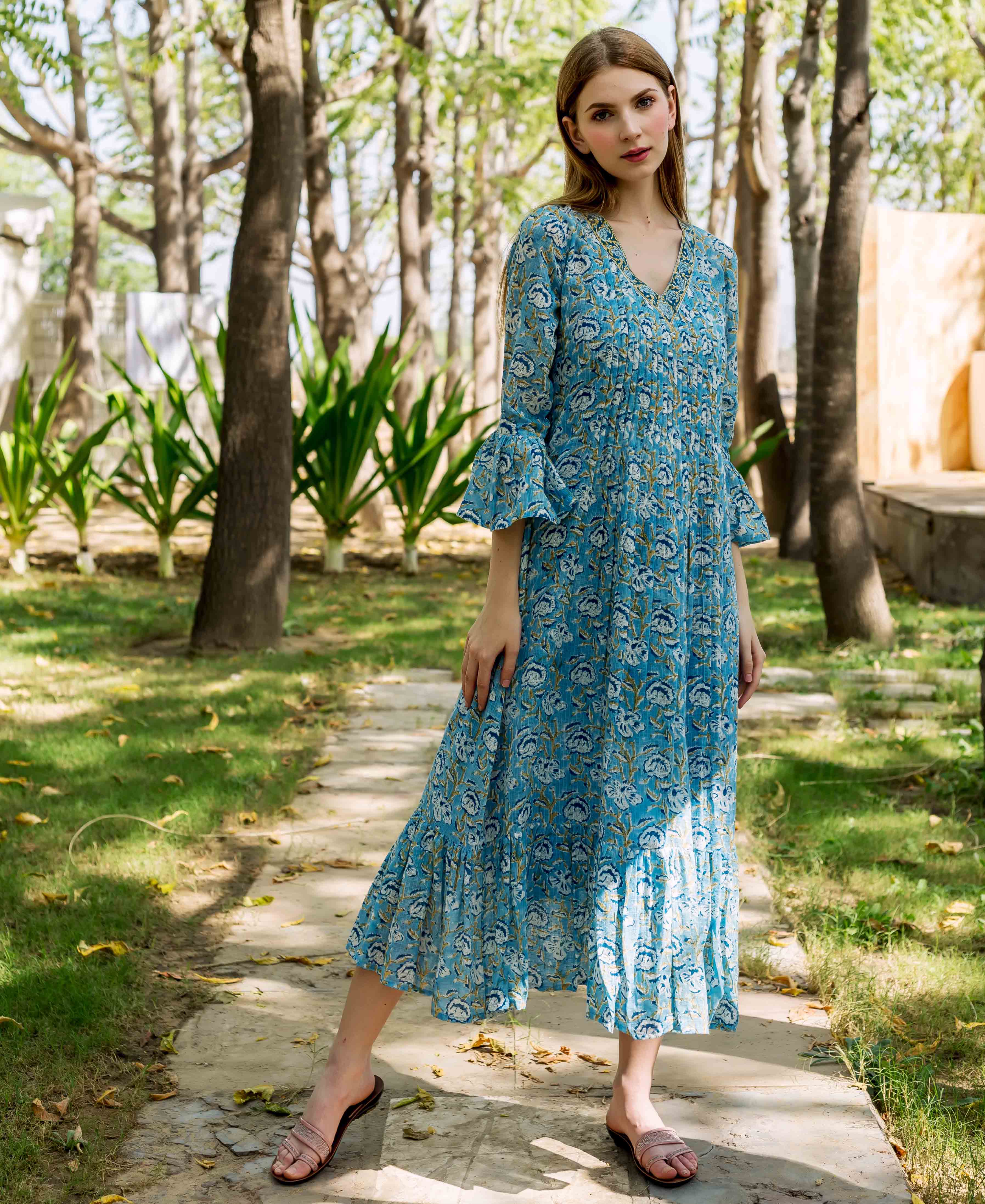 Model wears blue hand-block-printed floral Emily dress with V-neck and bell sleeves.
