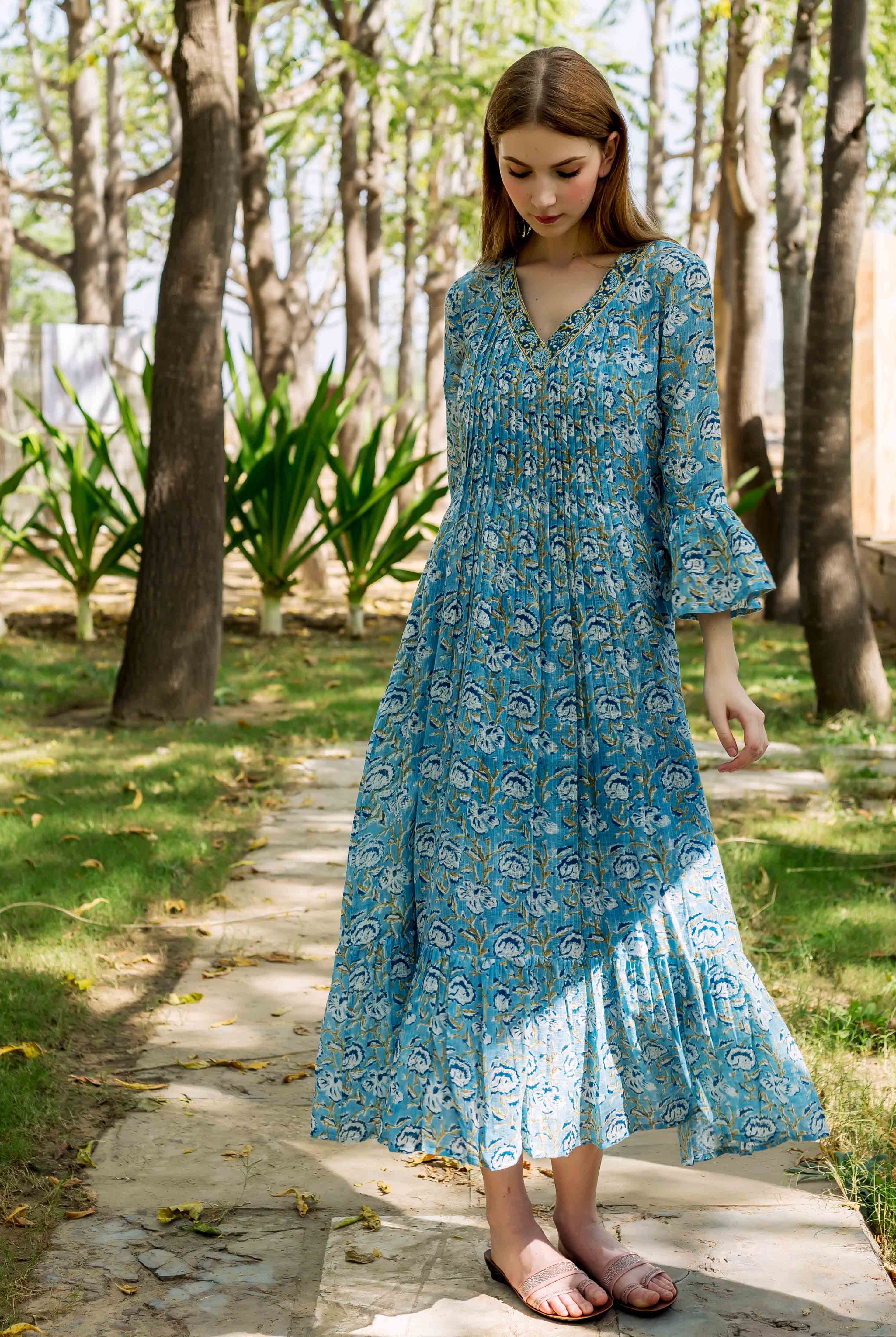 Model in a full-length blue hand-block printed floral dress with pleated bodice and bell sleeves.