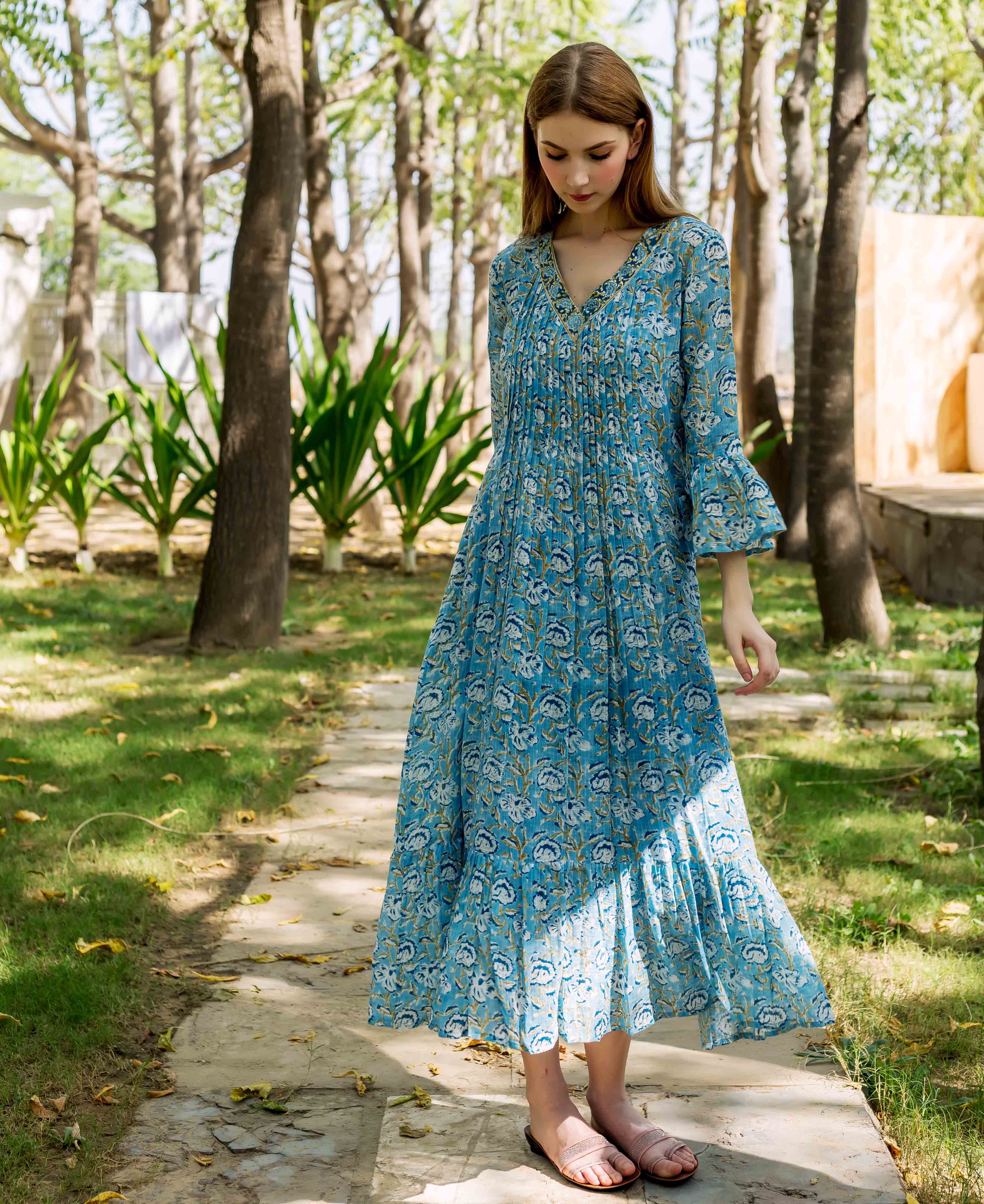 Model in a full-length blue hand-block printed floral dress with pleated bodice and bell sleeves.