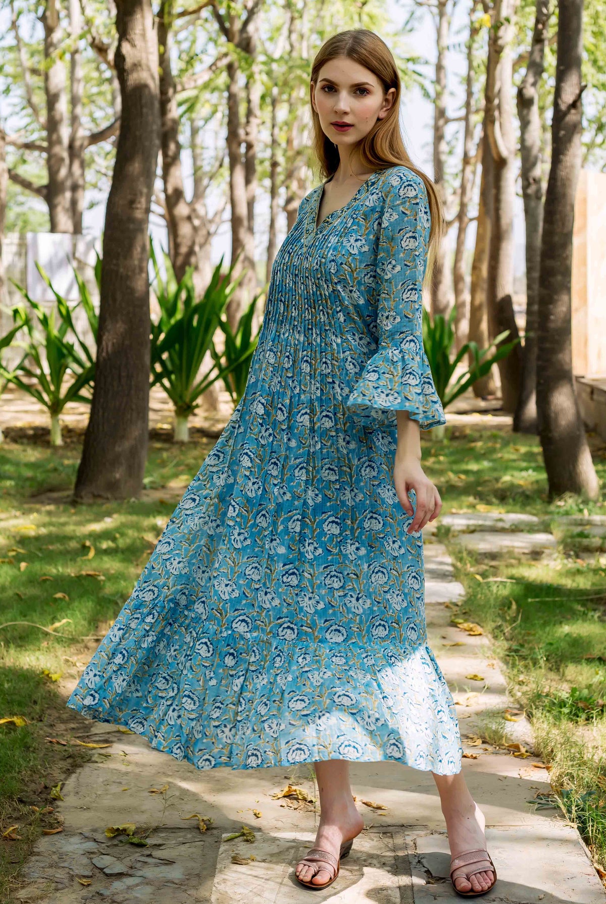 Model wearing a blue hand-block printed floral midi dress with pleated bodice and bell sleeves.