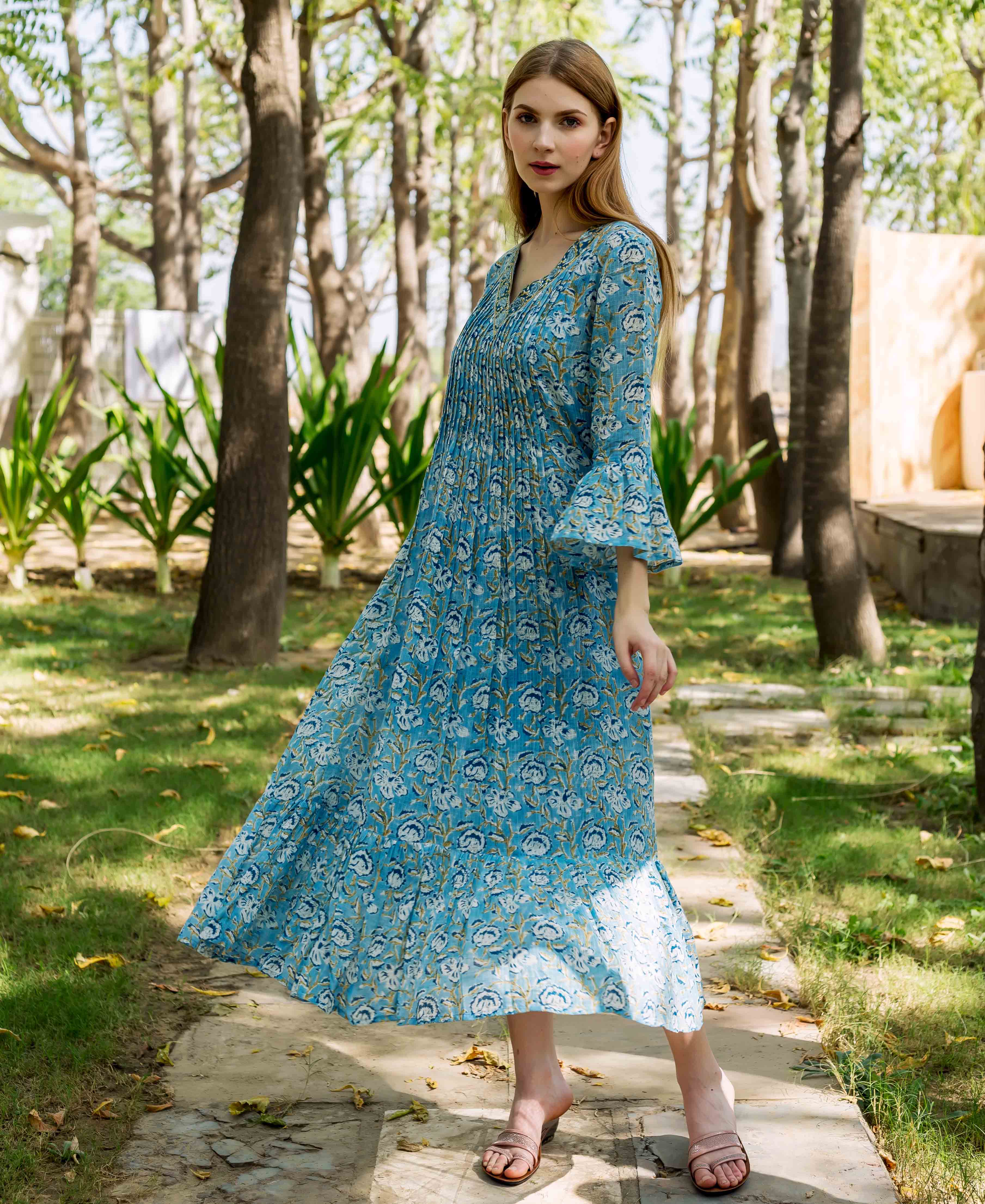 Model wearing a blue hand-block printed floral midi dress with pleated bodice and bell sleeves.