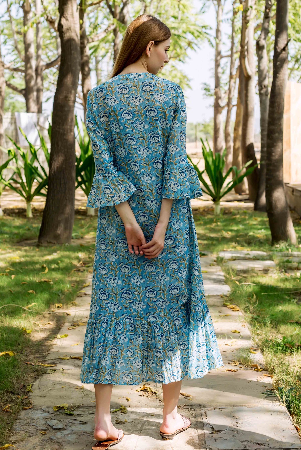 Model's back shows blue floral printed midi dress with bell sleeves and ruffled hem.