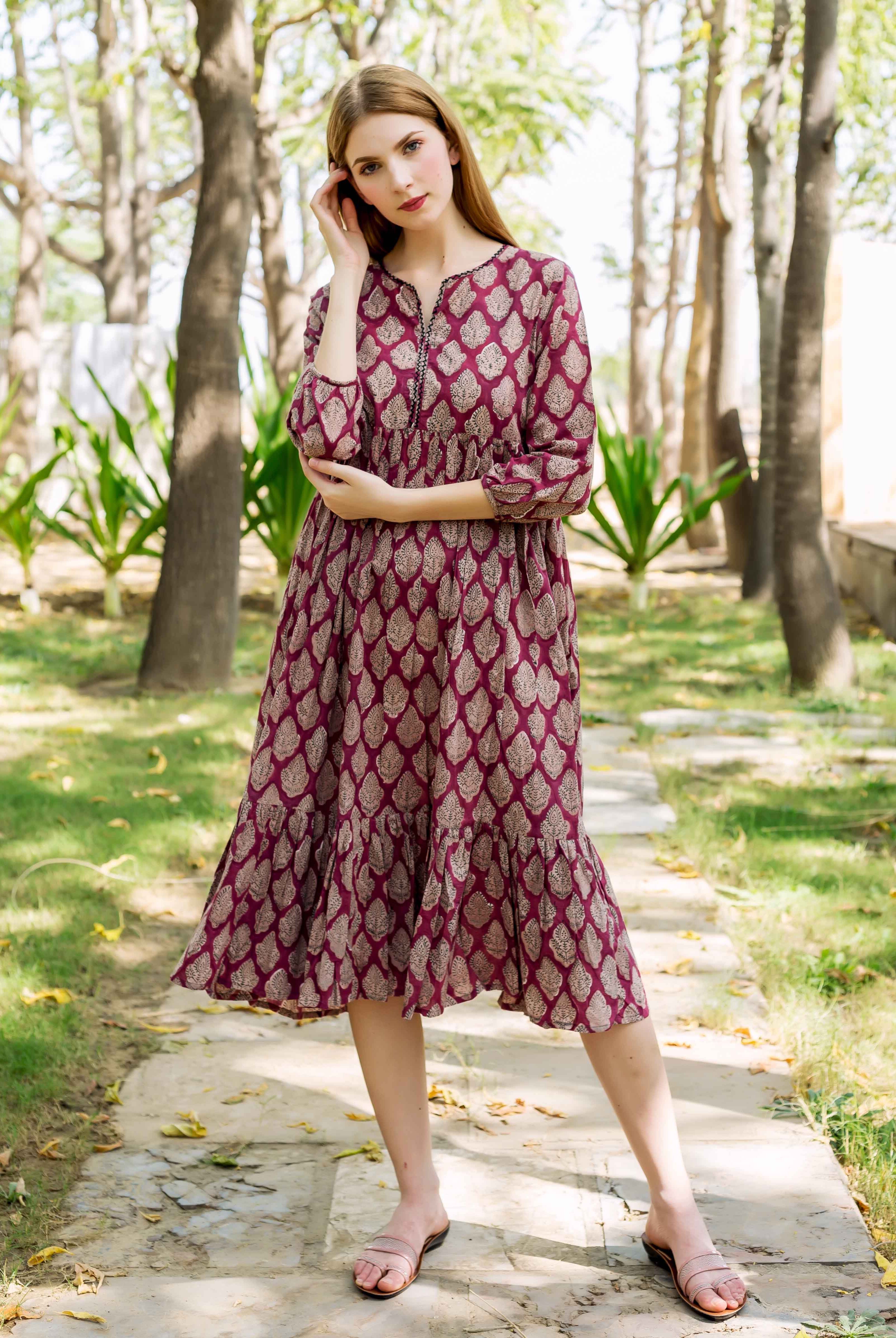 Model in a maroon hand-block-printed midi dress featuring gold leaf motifs and tiered hem.