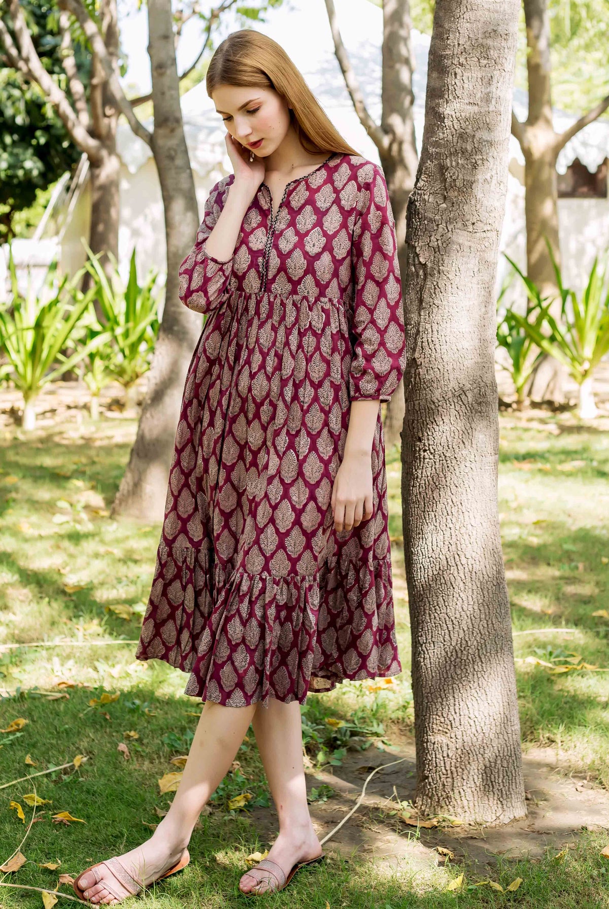 Model in full-length maroon Elizabeth printed dress with golden leaf pattern and ruffled hem.