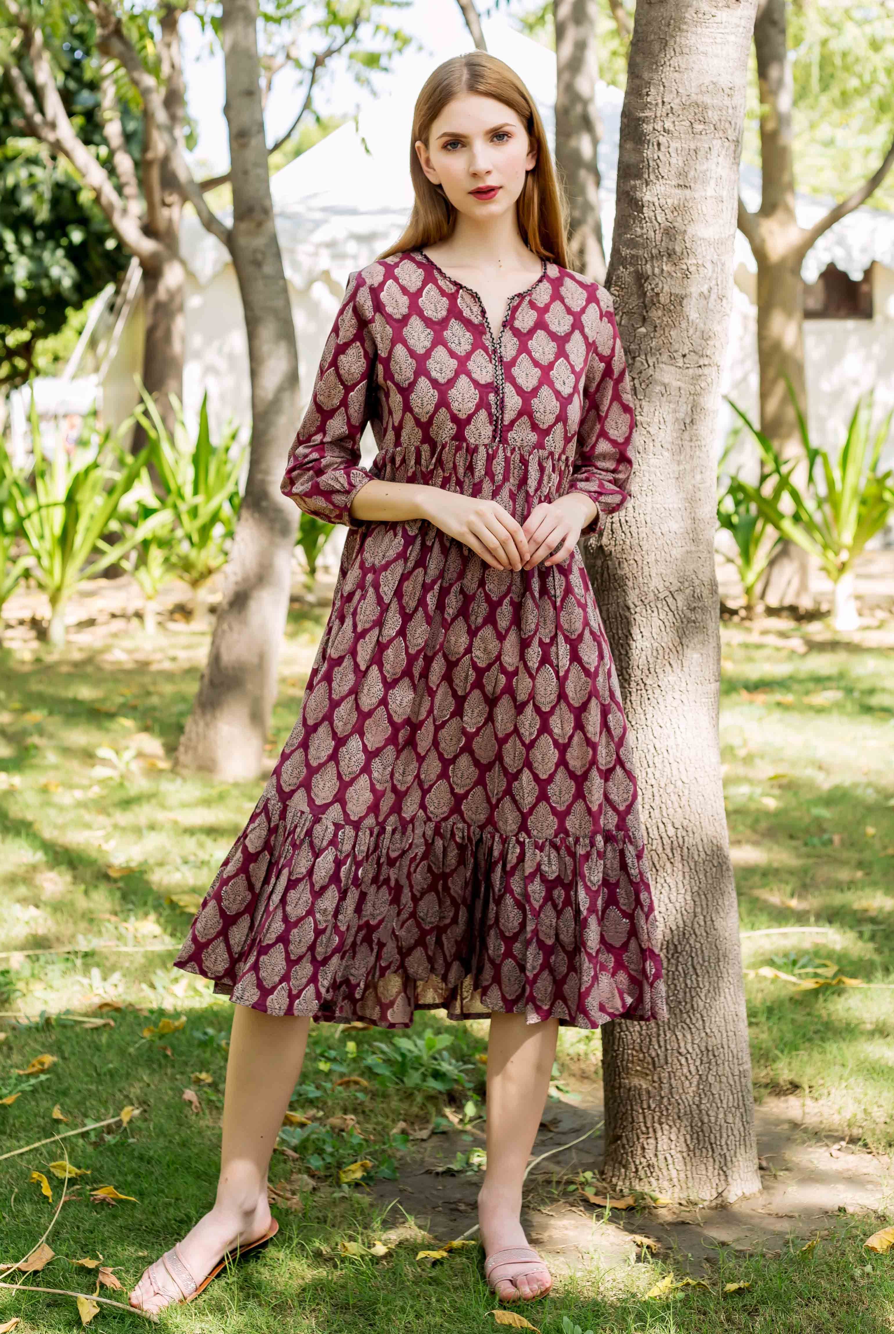 Model in a burgundy hand-block-printed midi dress featuring gold leaf patterns and ruffled hem.