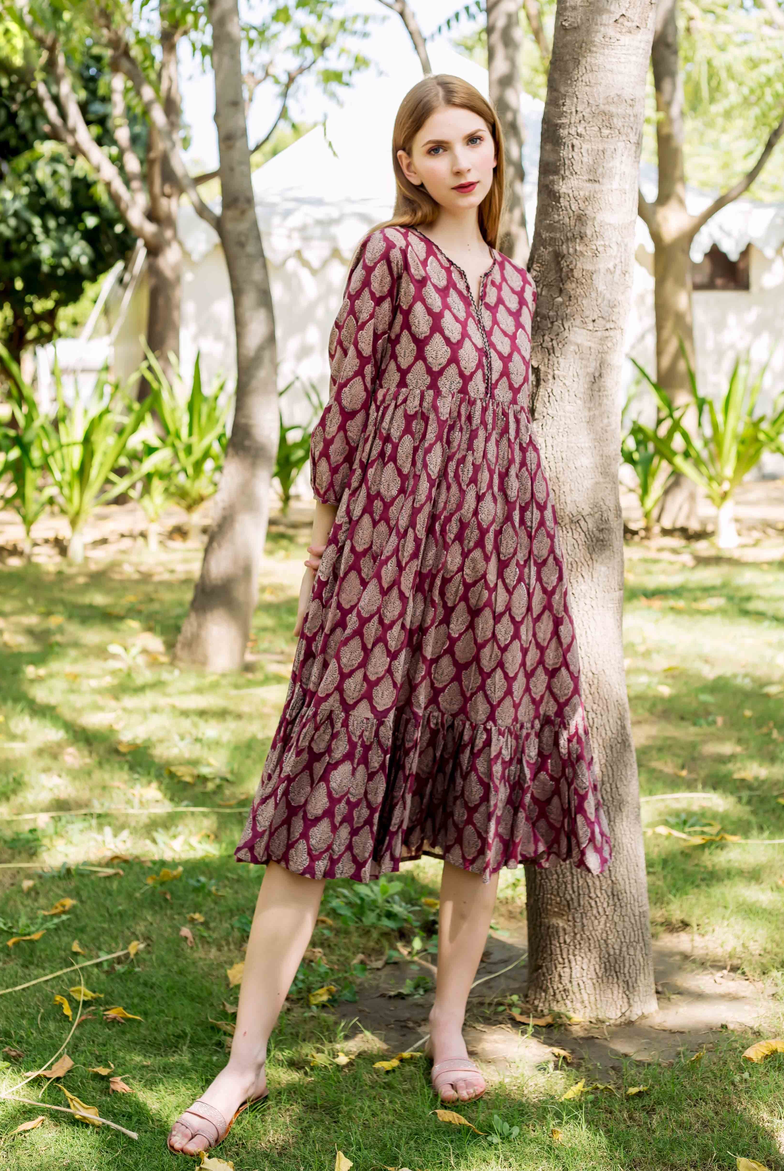 Front view of model wearing a maroon midi dress with a repeating golden leaf print.