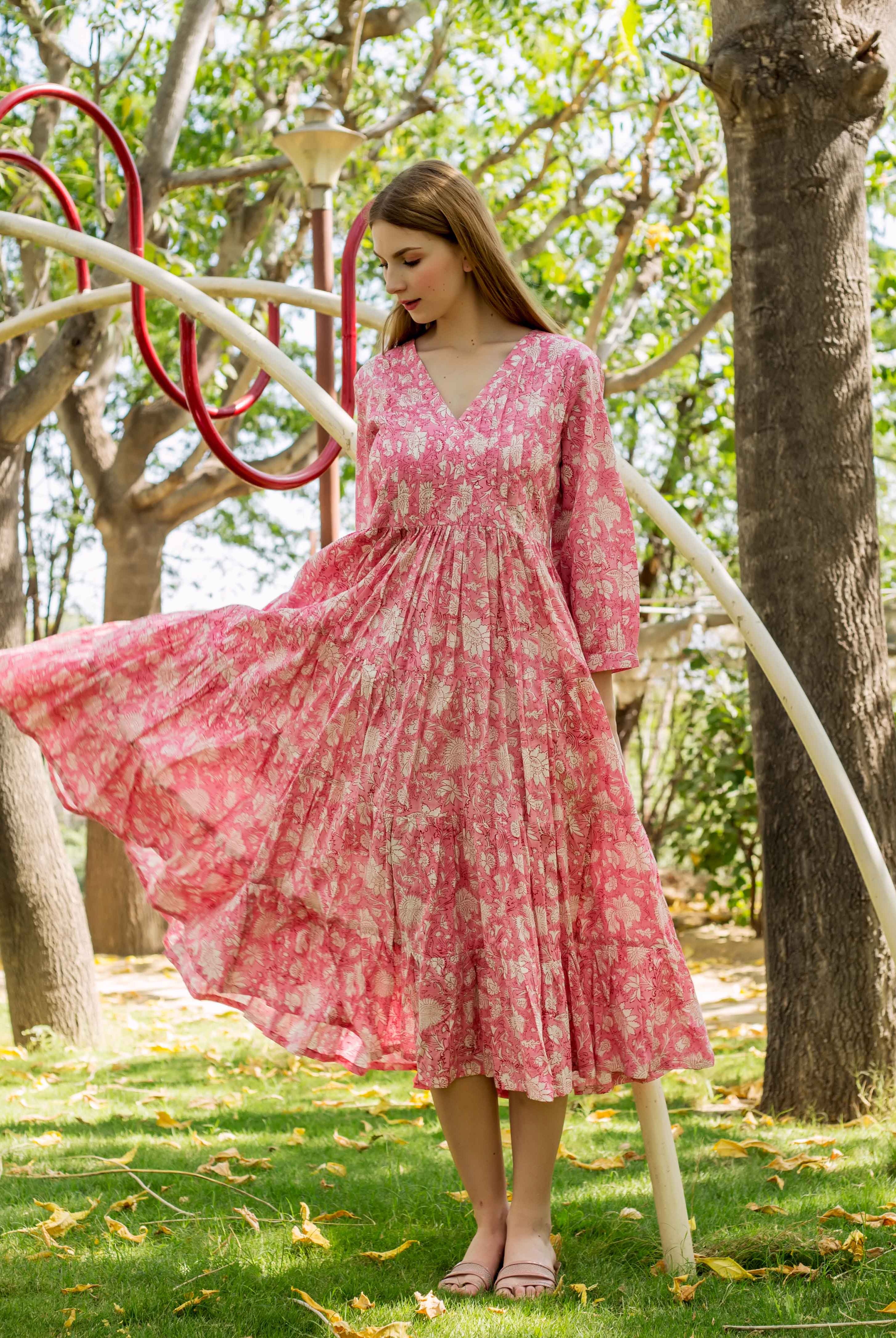 Model in a pink hand-block-printed ethnic dress with cream floral patterns, skirt flowing outdoors.