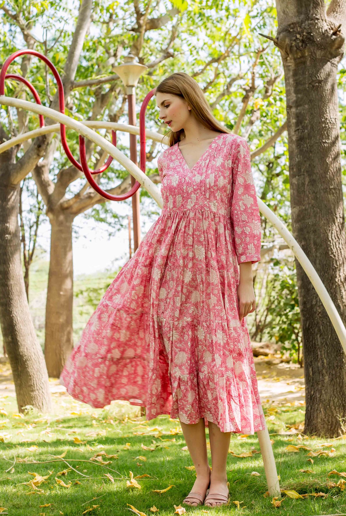 Model wearing a pink hand-block-printed floral V-neck midi dress outdoors.
