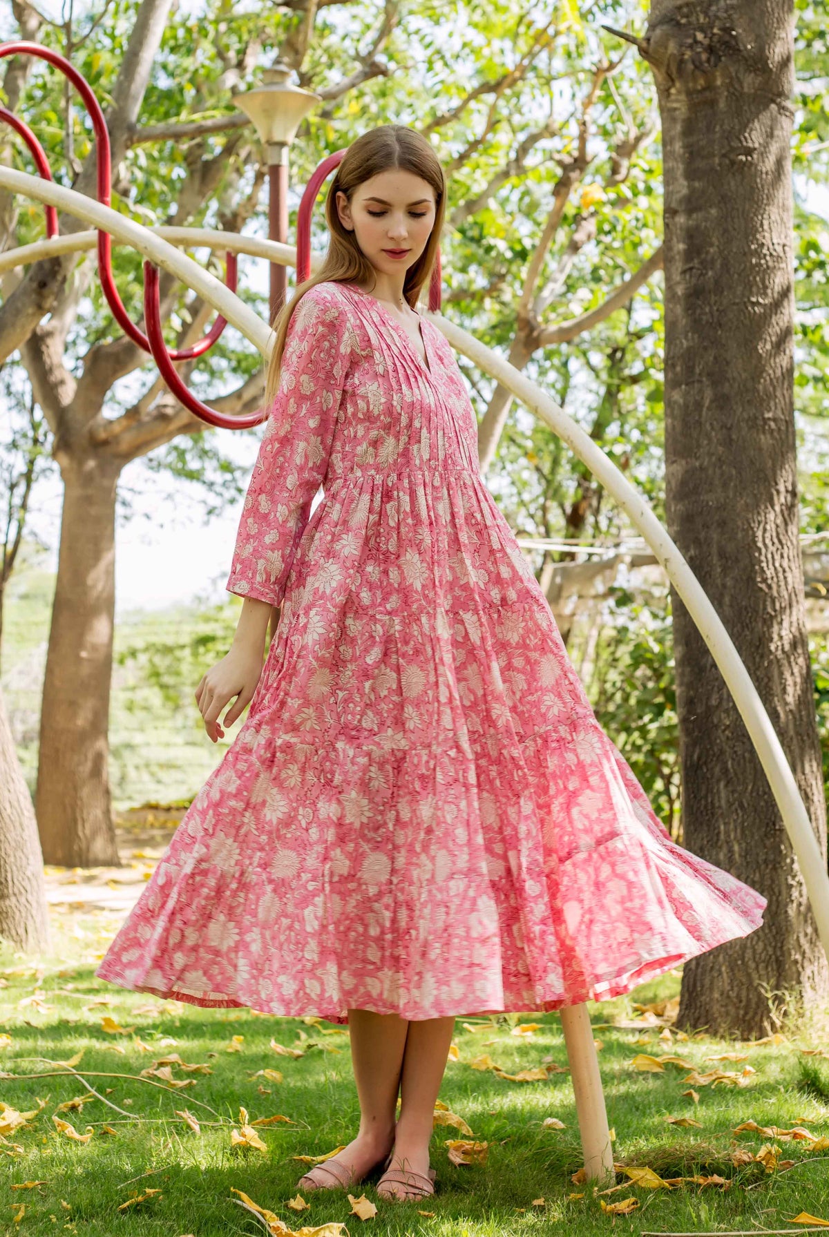 Model in a pink hand-block-printed floral tiered midi dress with full skirt outside.