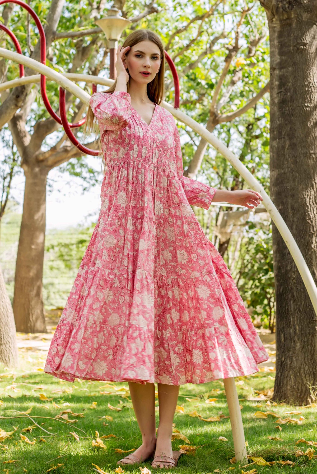 Model poses in a pink hand-block-printed V-neck tiered dress with white floral patterns.