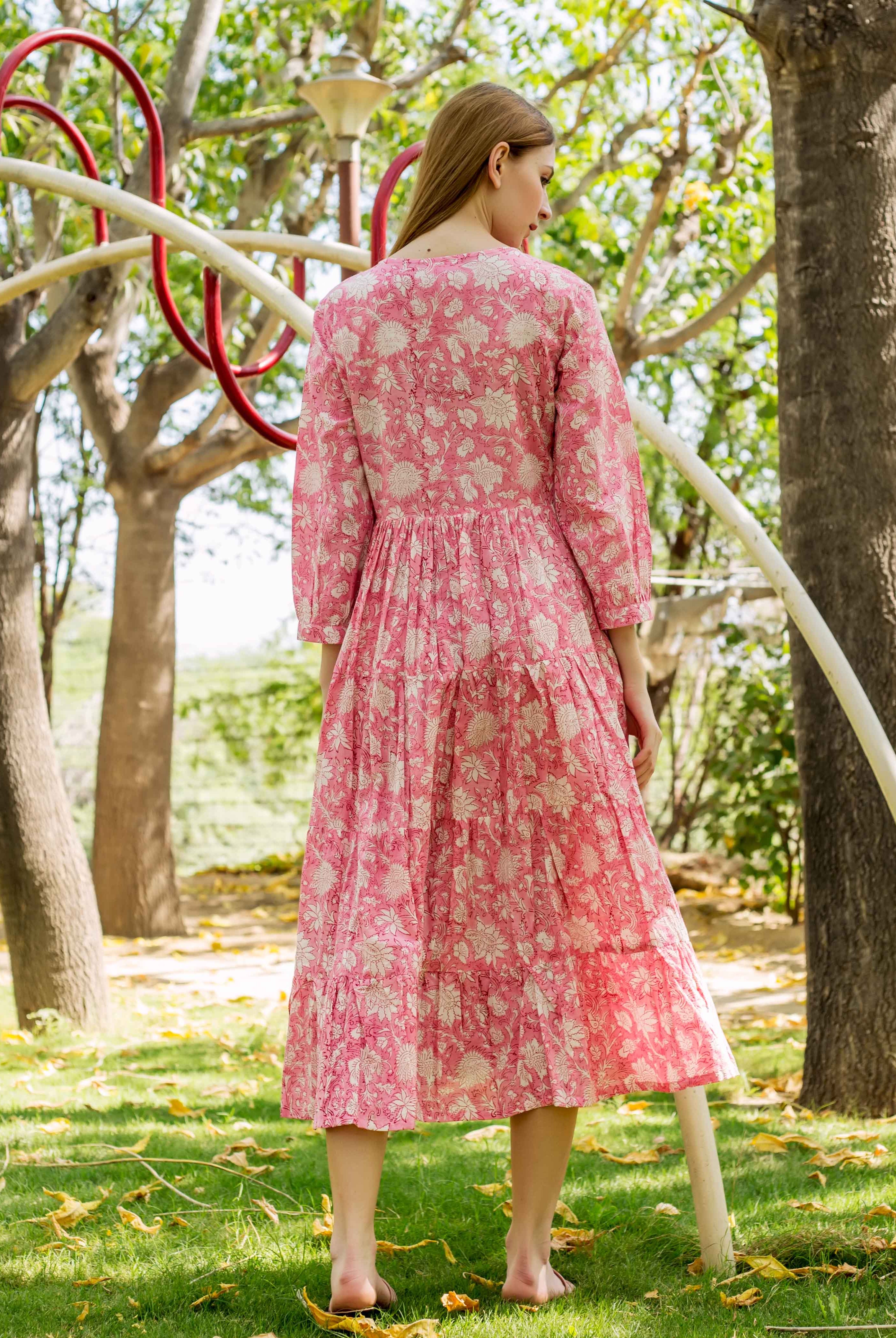 Rear view of model wearing a pink tiered midi dress with cream floral print outdoors.
