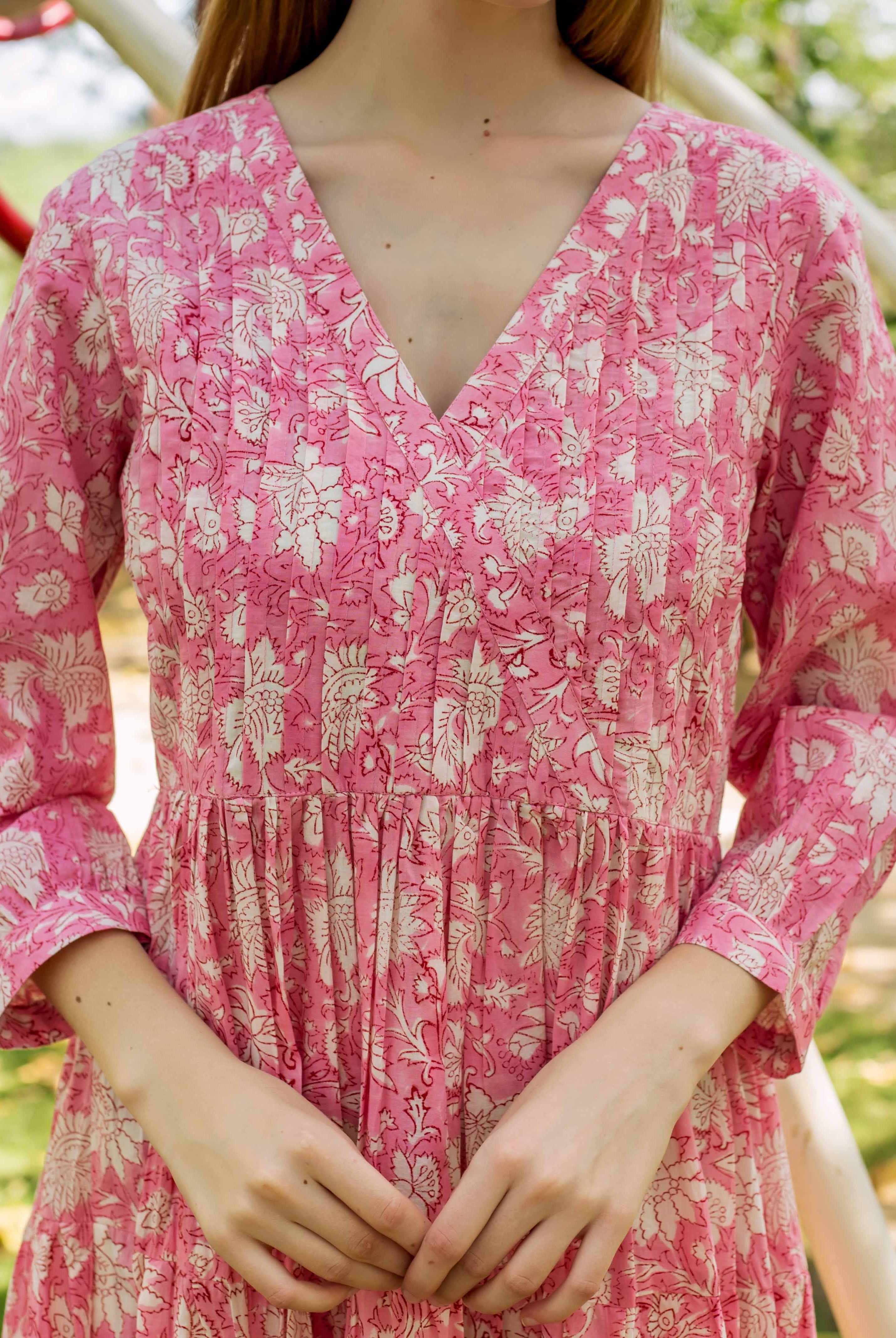 Pink V-neck hand-block floral print dress with pintucks and gathered waist on model.