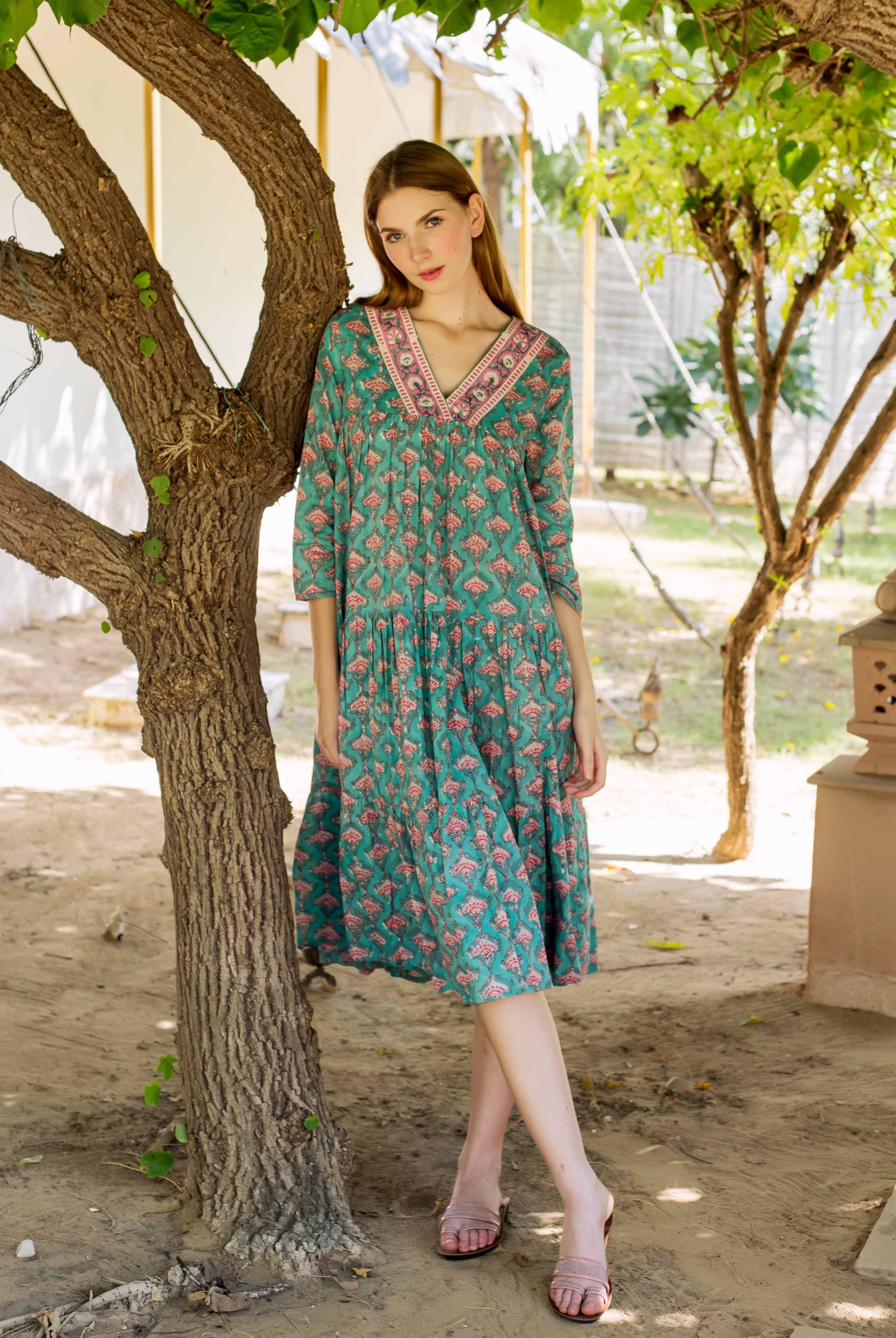 Front view of a model in a teal tiered dress with pink hand-block-printed ethnic motifs.