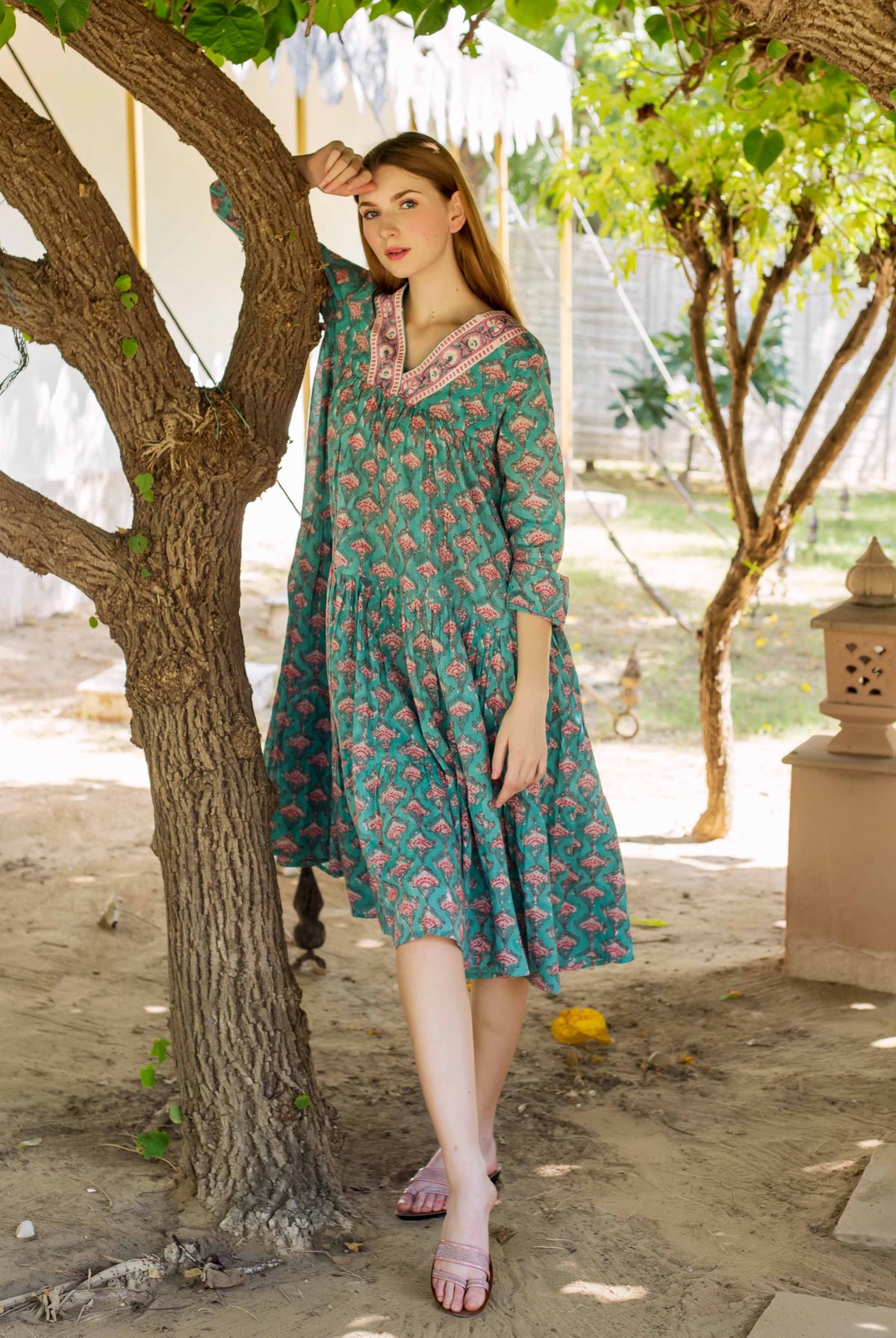 Female model in a teal green tiered, hand-block-printed dress with pink floral motifs.