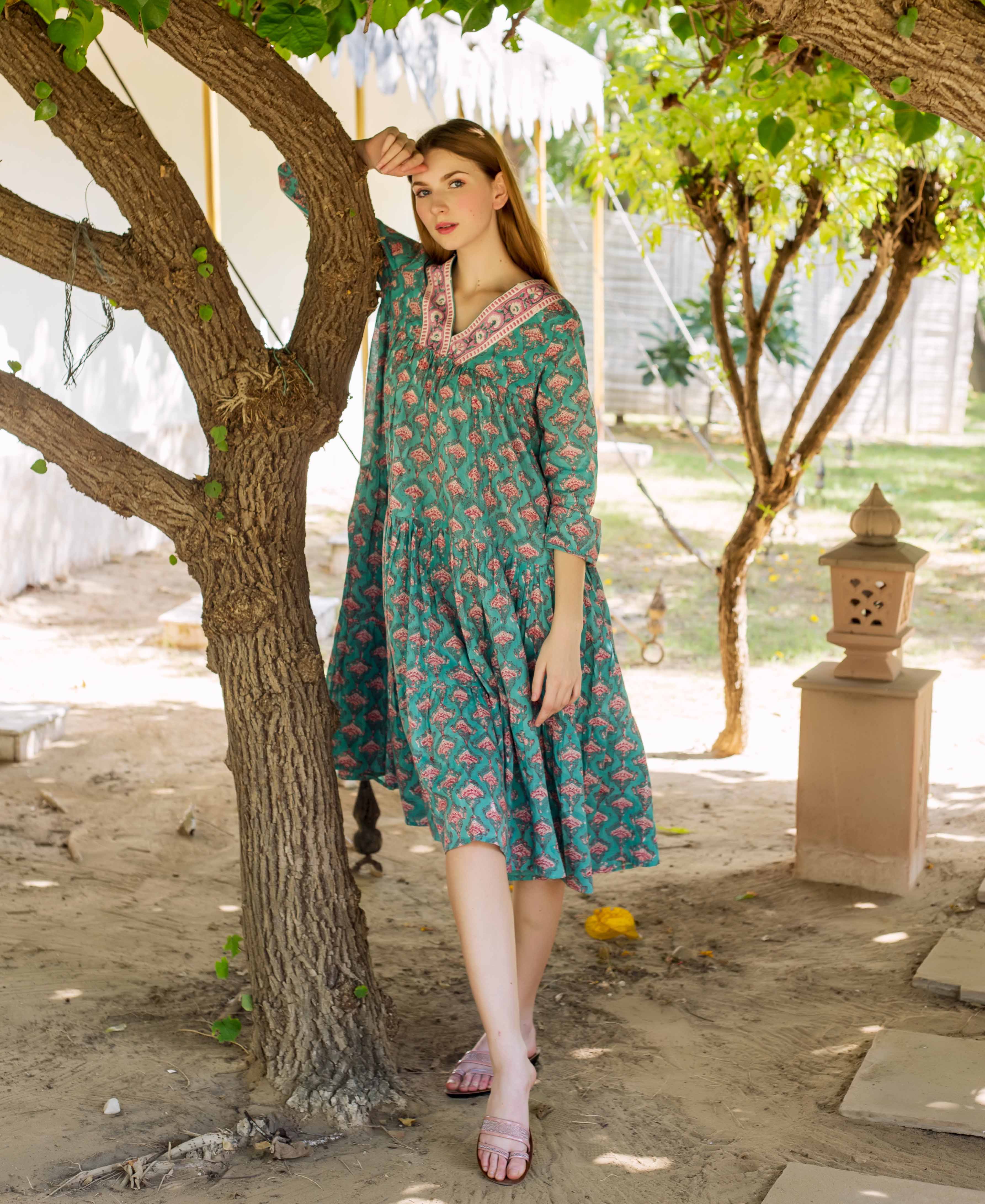 Female model in a teal green tiered, hand-block-printed dress with pink floral motifs.