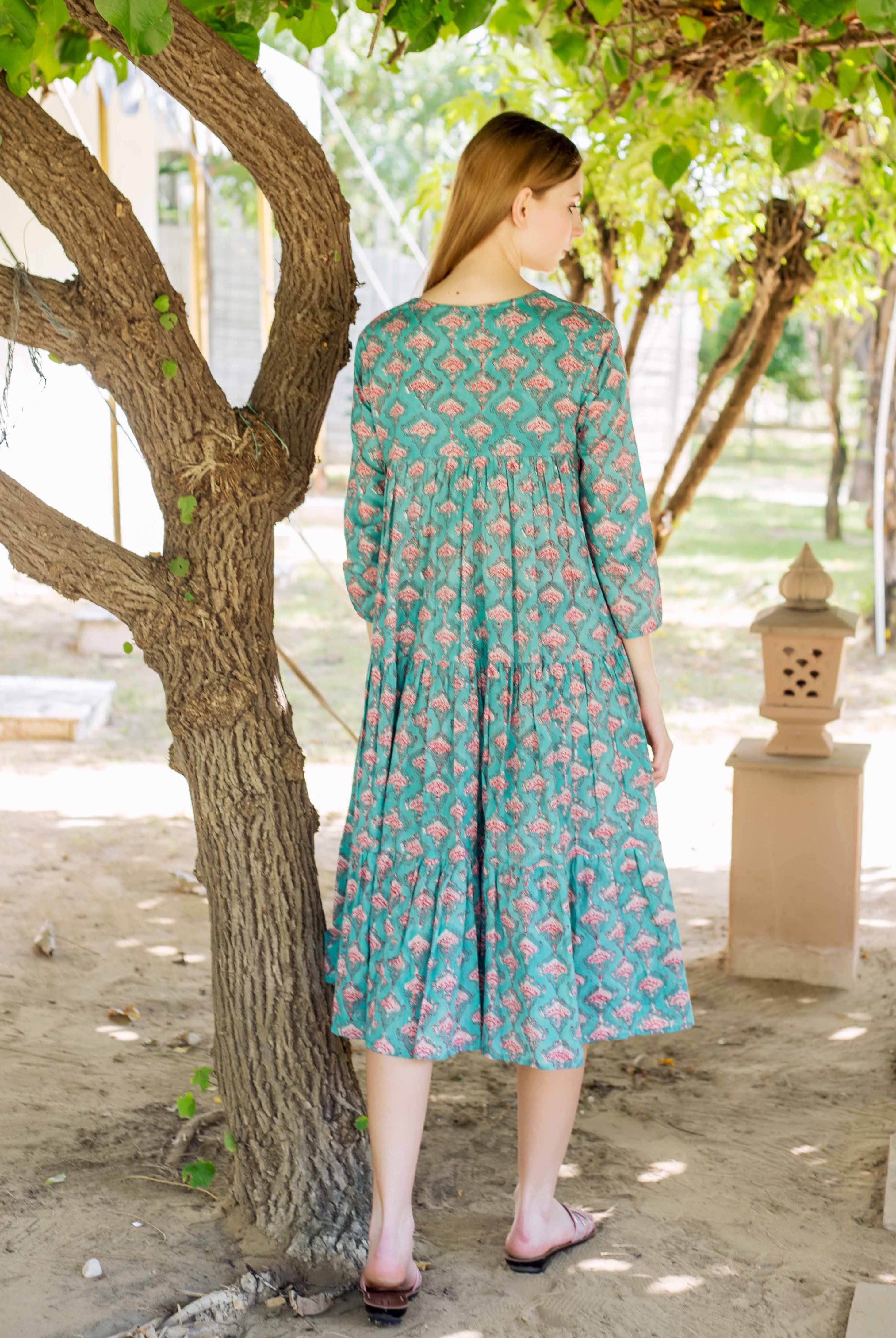 Back view of a model wearing a teal green tiered midi dress with pink ethnic print.