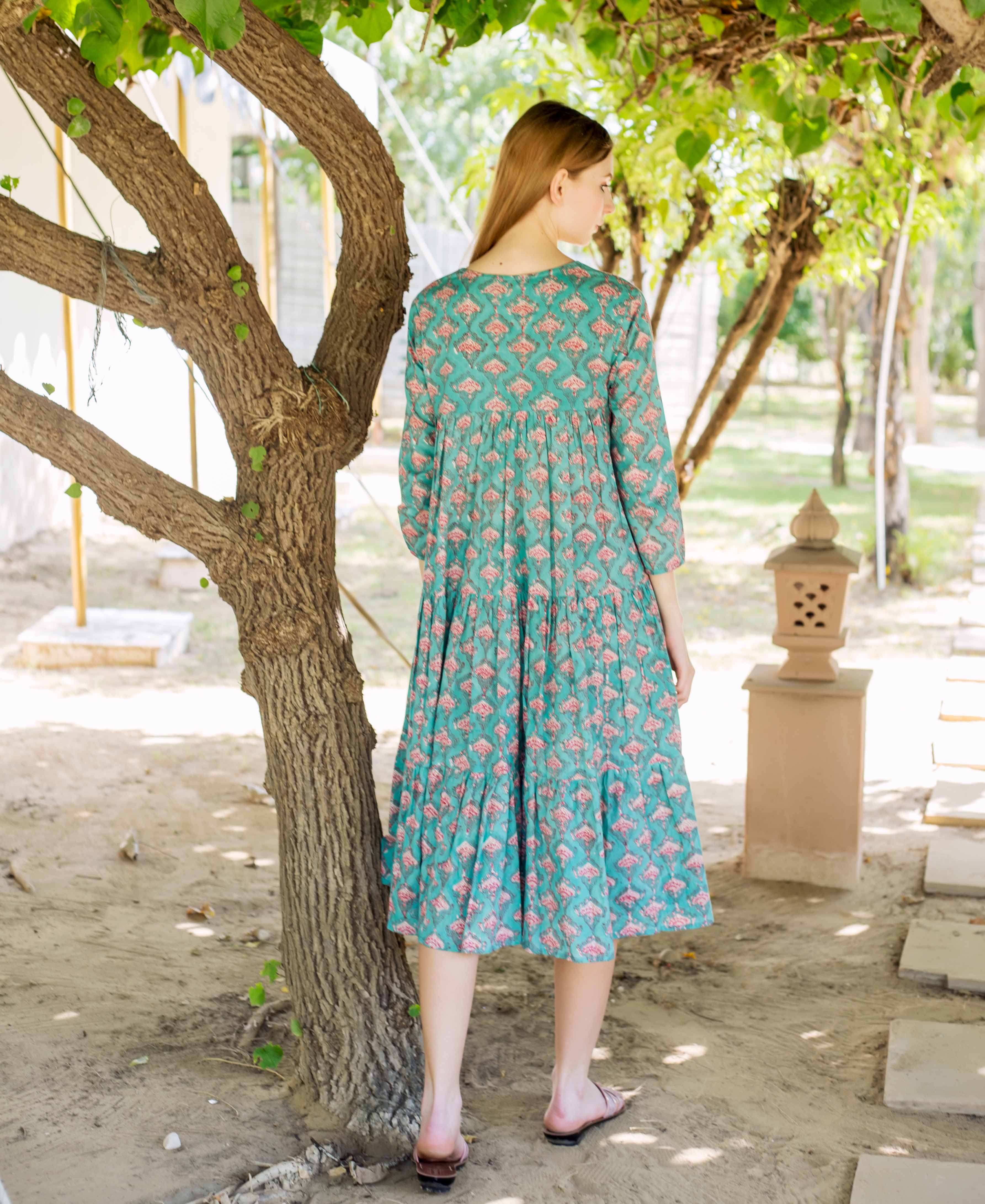 Back view of a model wearing a teal green tiered midi dress with pink ethnic print.